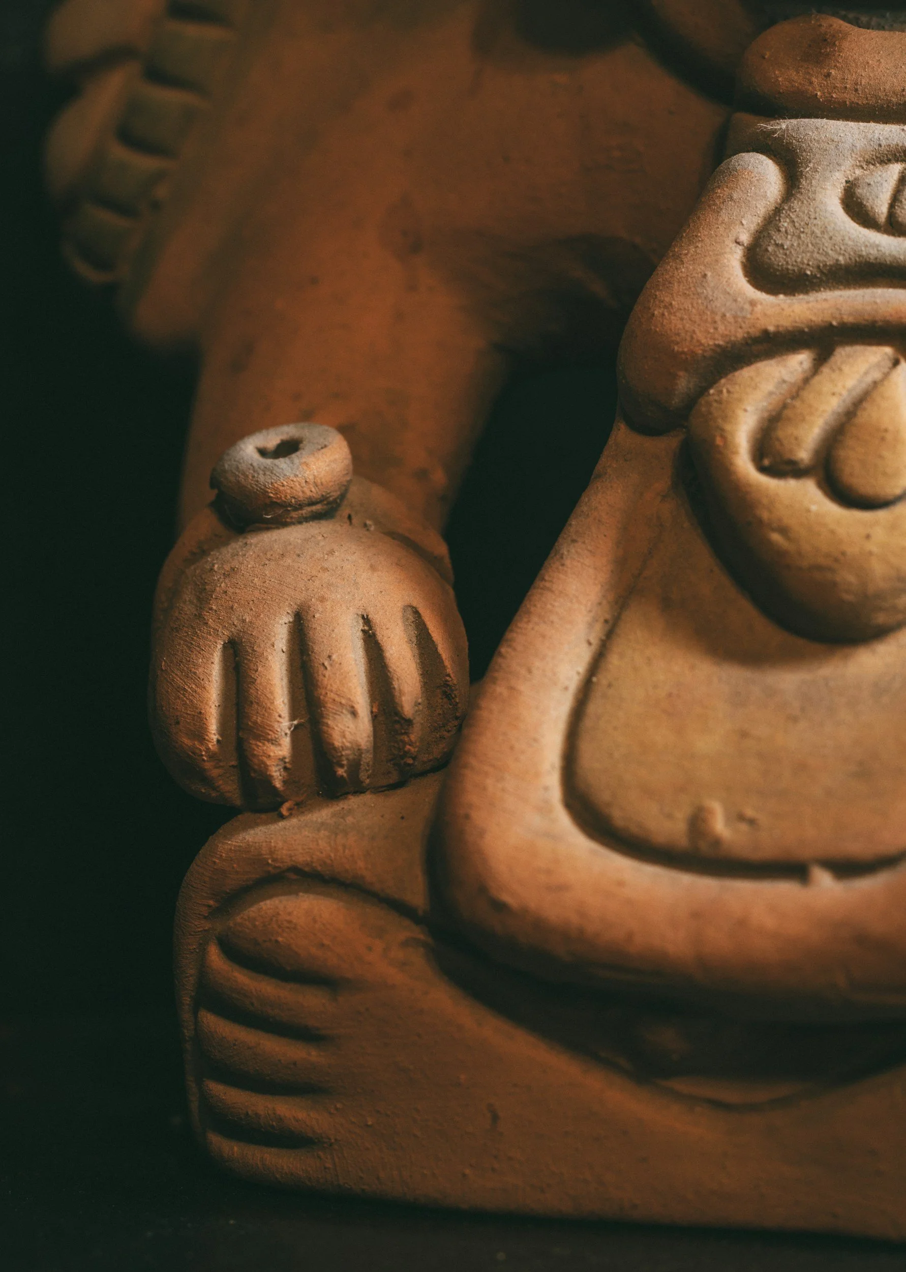 Close-up of a Central American terracotta sculpture showing part of a face with a prominent nose and a textured hand resting on the body, highlighting detailed craftsmanship.