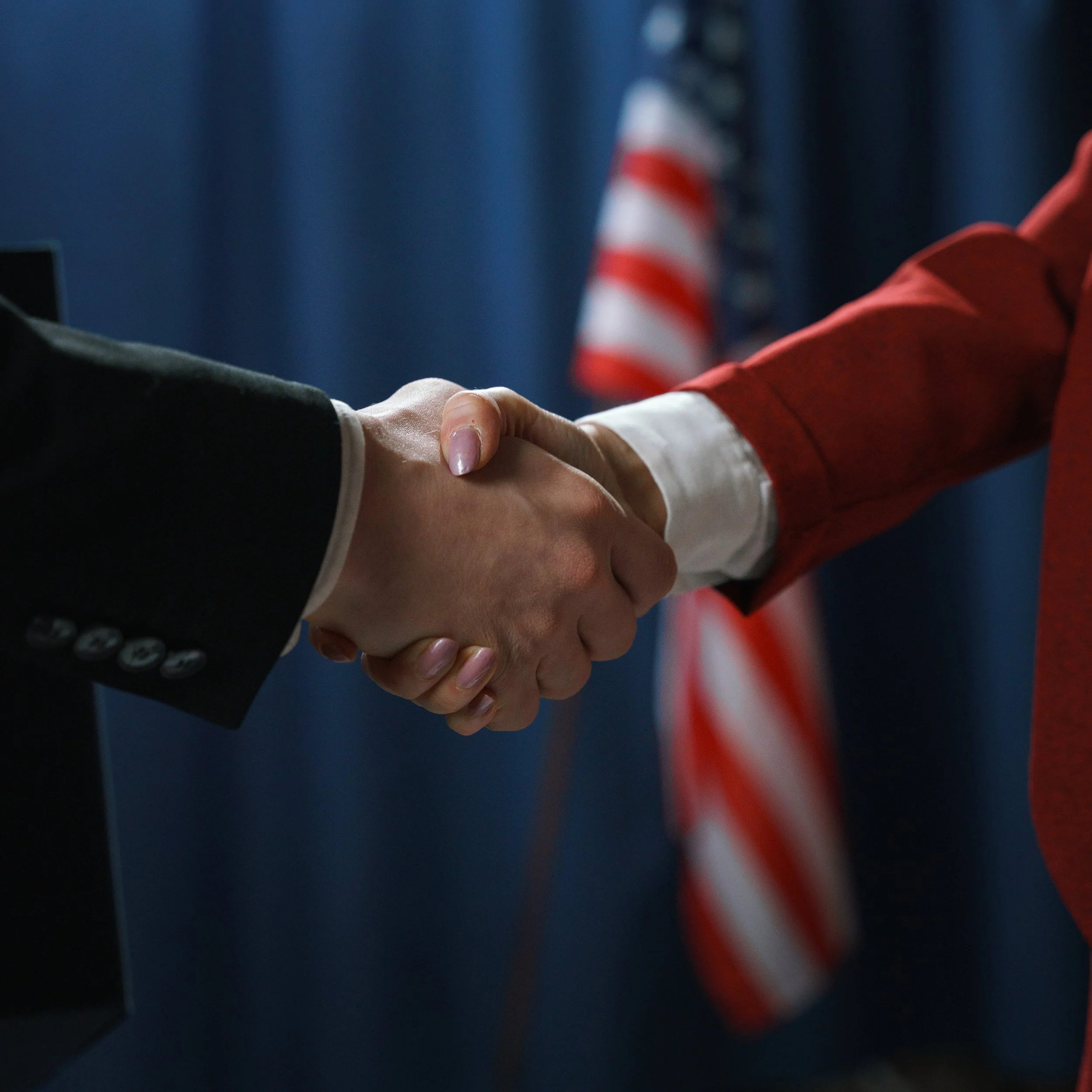 Two people shaking hands with an American flag in the background.