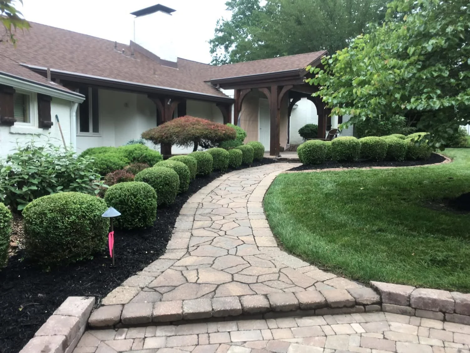 Limestone pathway leading to a house with a covered porch, surrounded by neatly trimmed bushes and a well-maintained lawn.