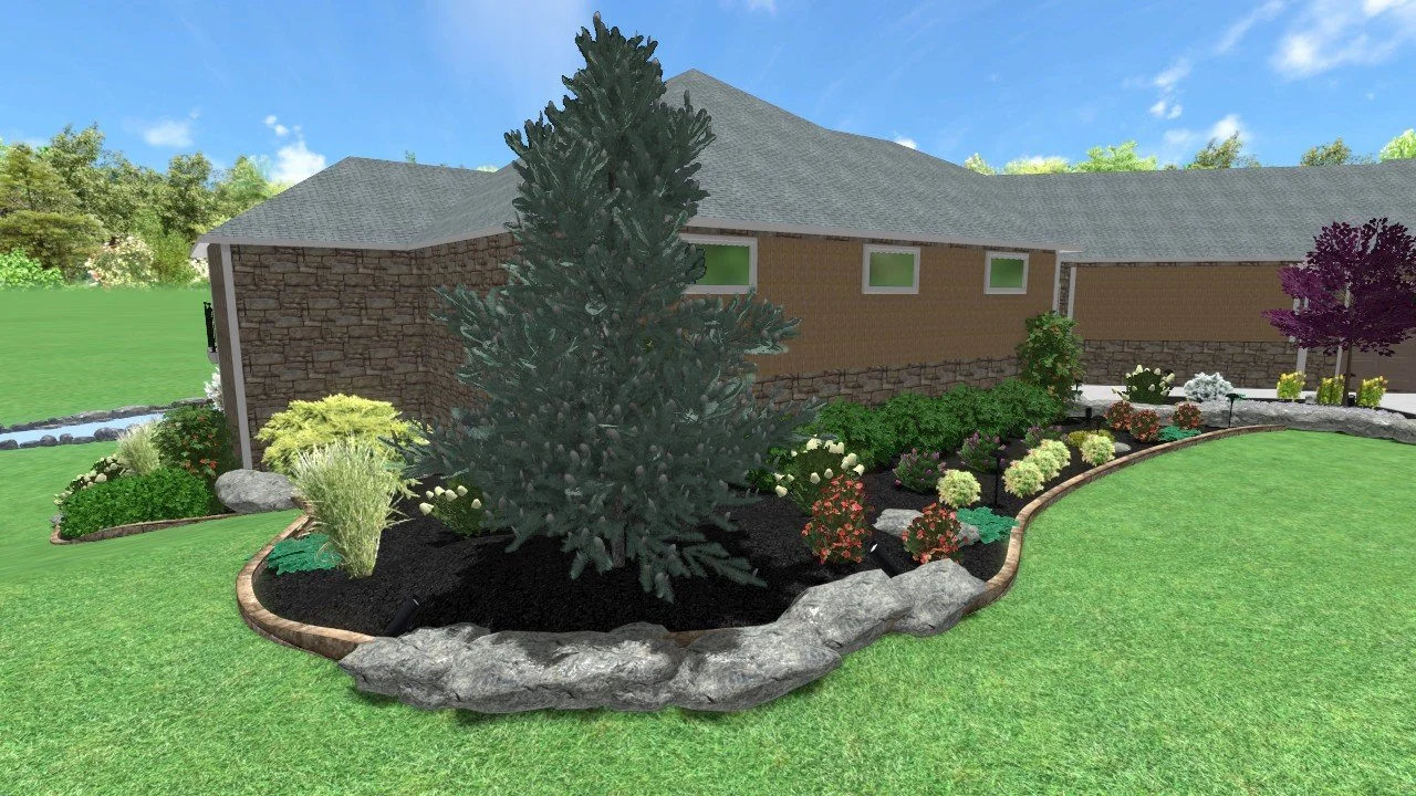 A landscaped backyard garden with a large pine tree surrounded by various shrubs and flowering plants, bordered by rocks and housed next to a house with brown brick and stone walls under a blue sky with some clouds.