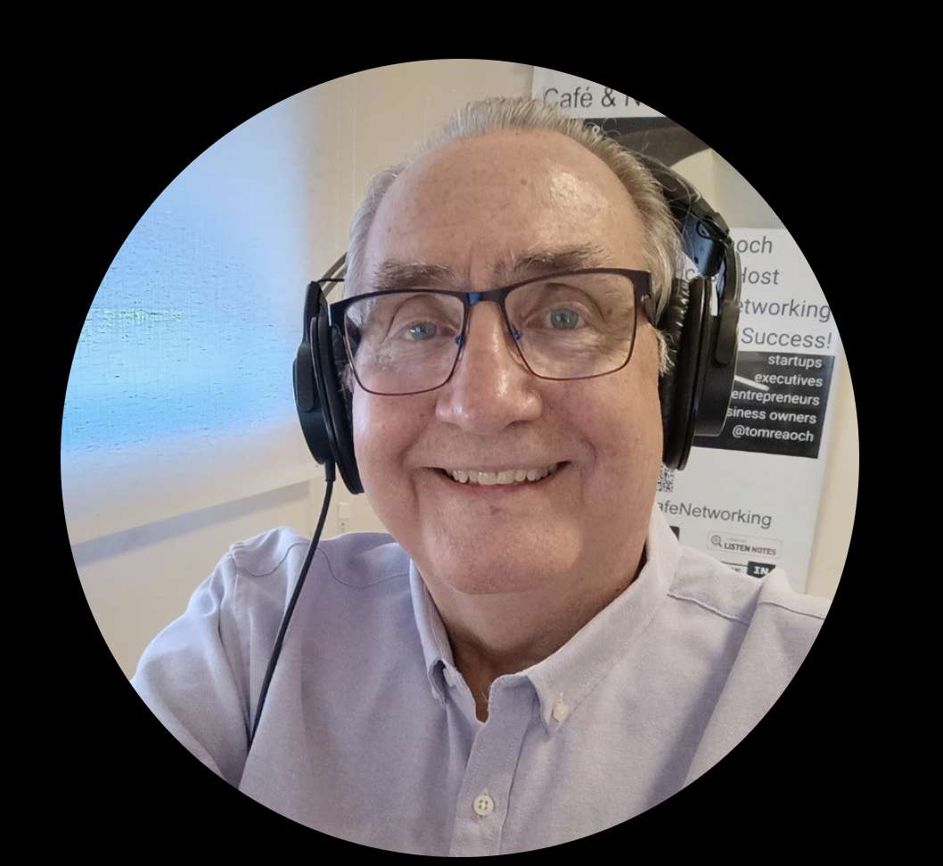 Man with glasses and headset smiling in an office, with a white shirt and a poster in the background.