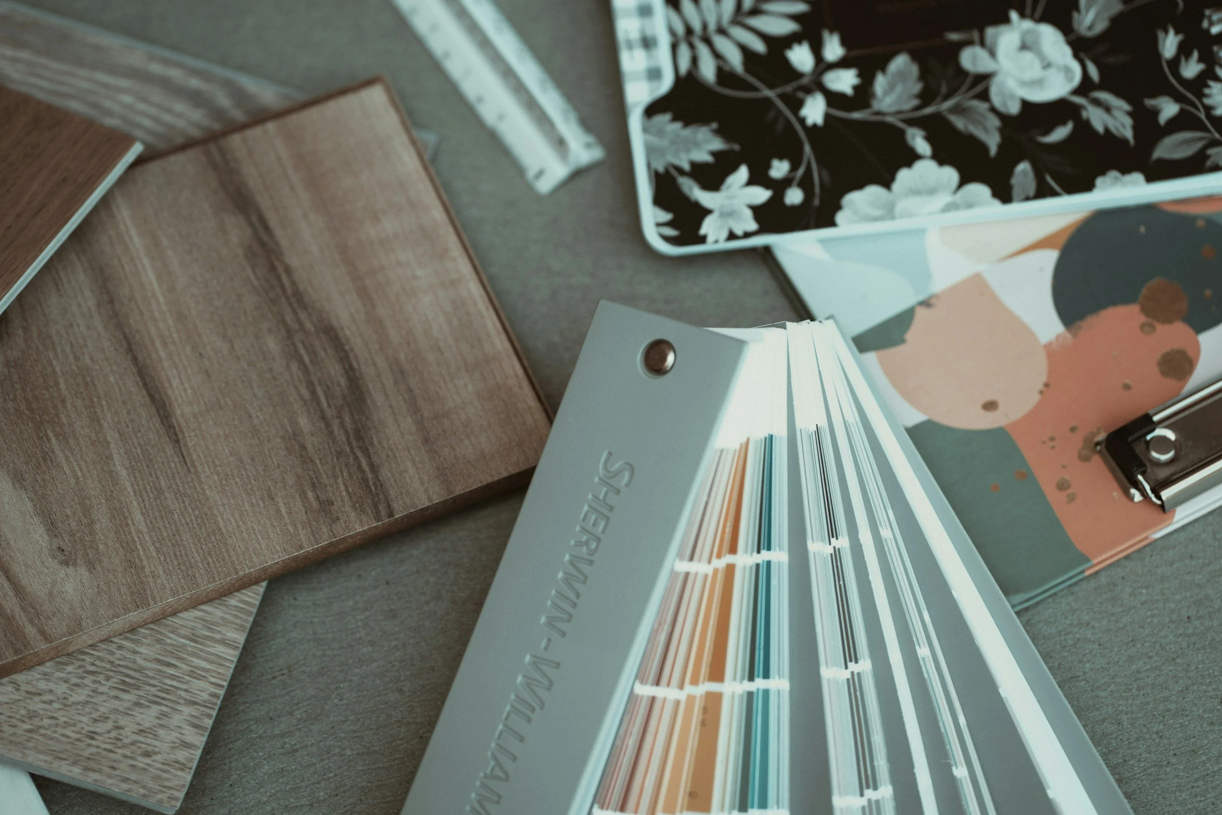 A color sample fan deck, several wood finish sample boards, and decorative trays with floral and abstract patterns are displayed on a table.