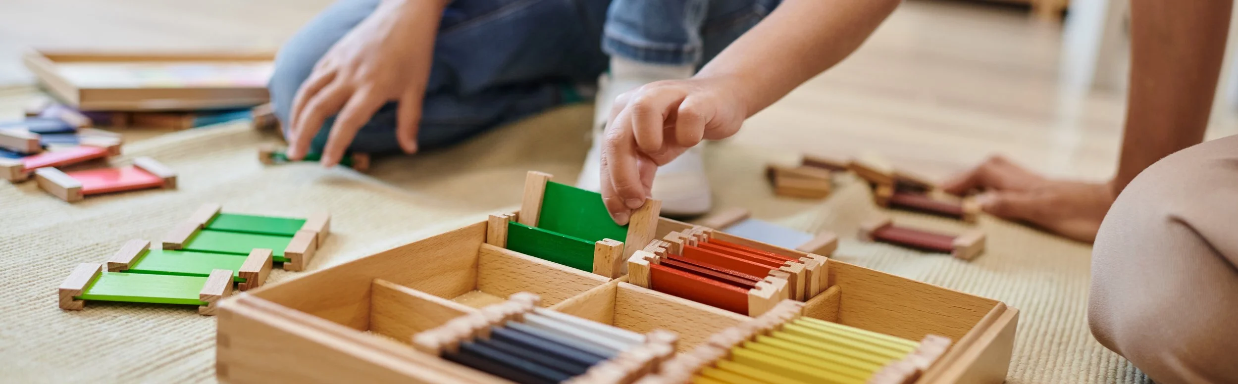 Children playing with colorful wooden tiles and a wooden storage box on a woven mat.