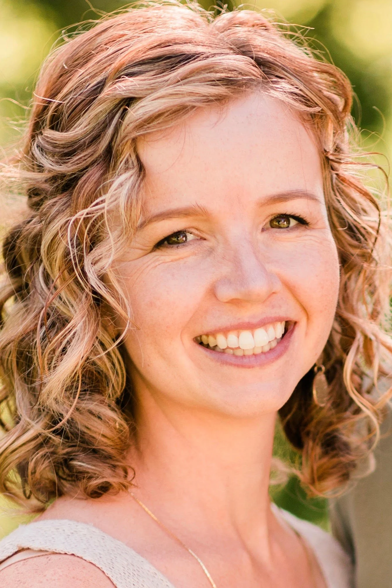 Close-up of a smiling woman with curly blonde hair outdoors.