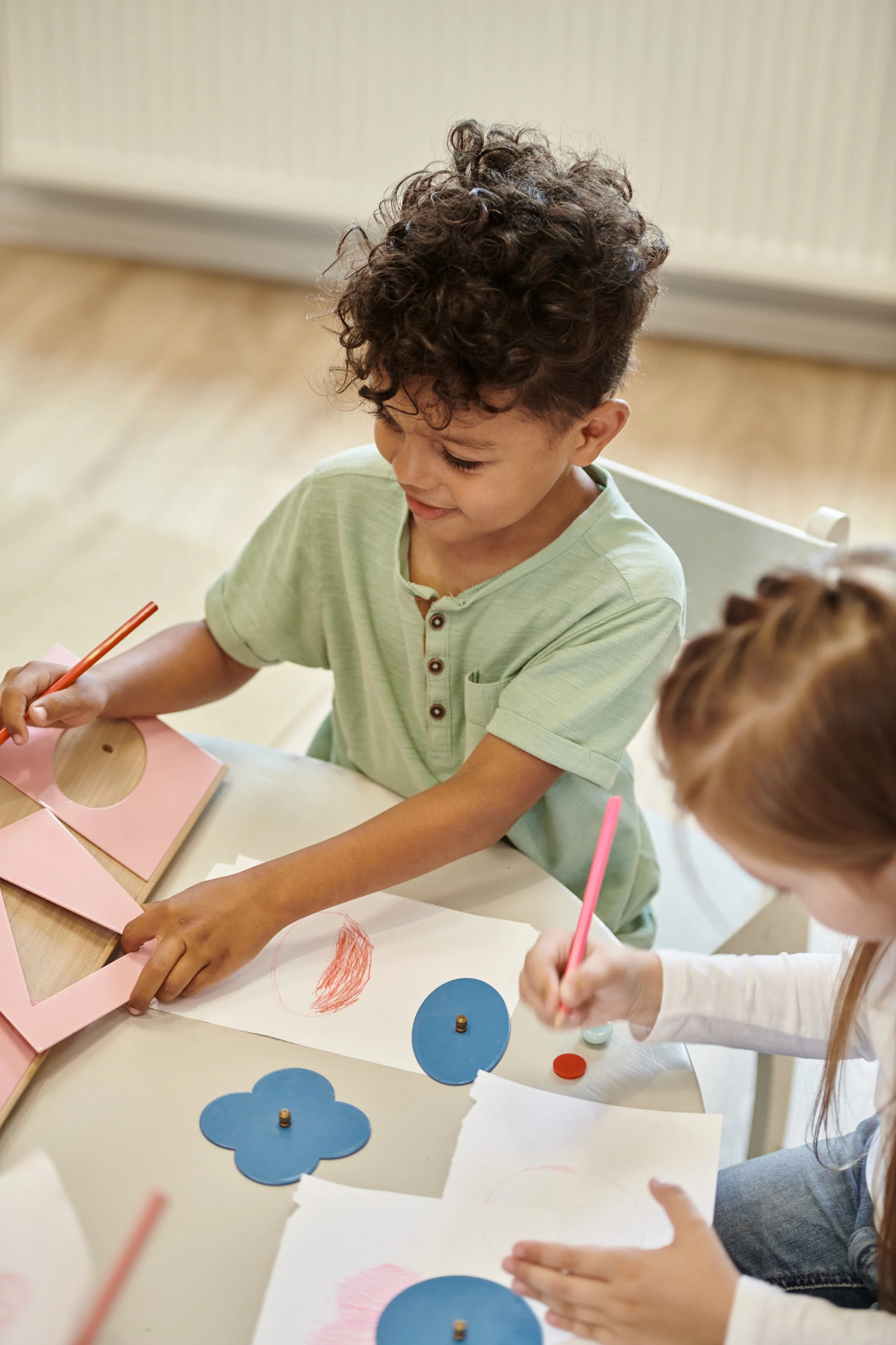 Children seated at a table working on craft projects with colored paper, markers, and paper cut-outs.