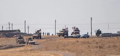 Military convoy with tanks, trucks, and personnel moving across a grassy field.