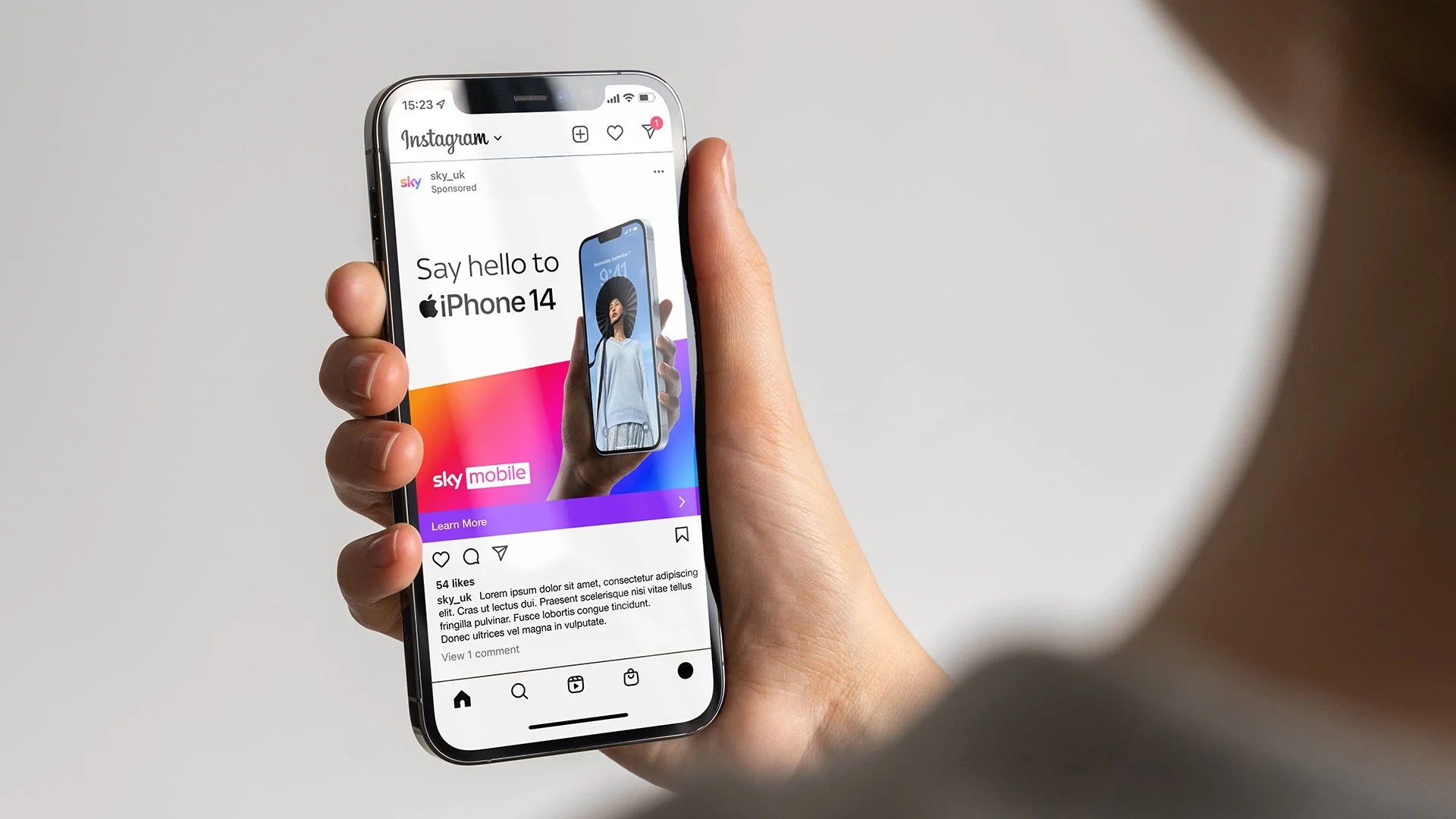 Close-up of a person holding a smartphone displaying an Instagram advertisement for the iPhone 14 with colorful graphics and a woman holding the phone in the ad.