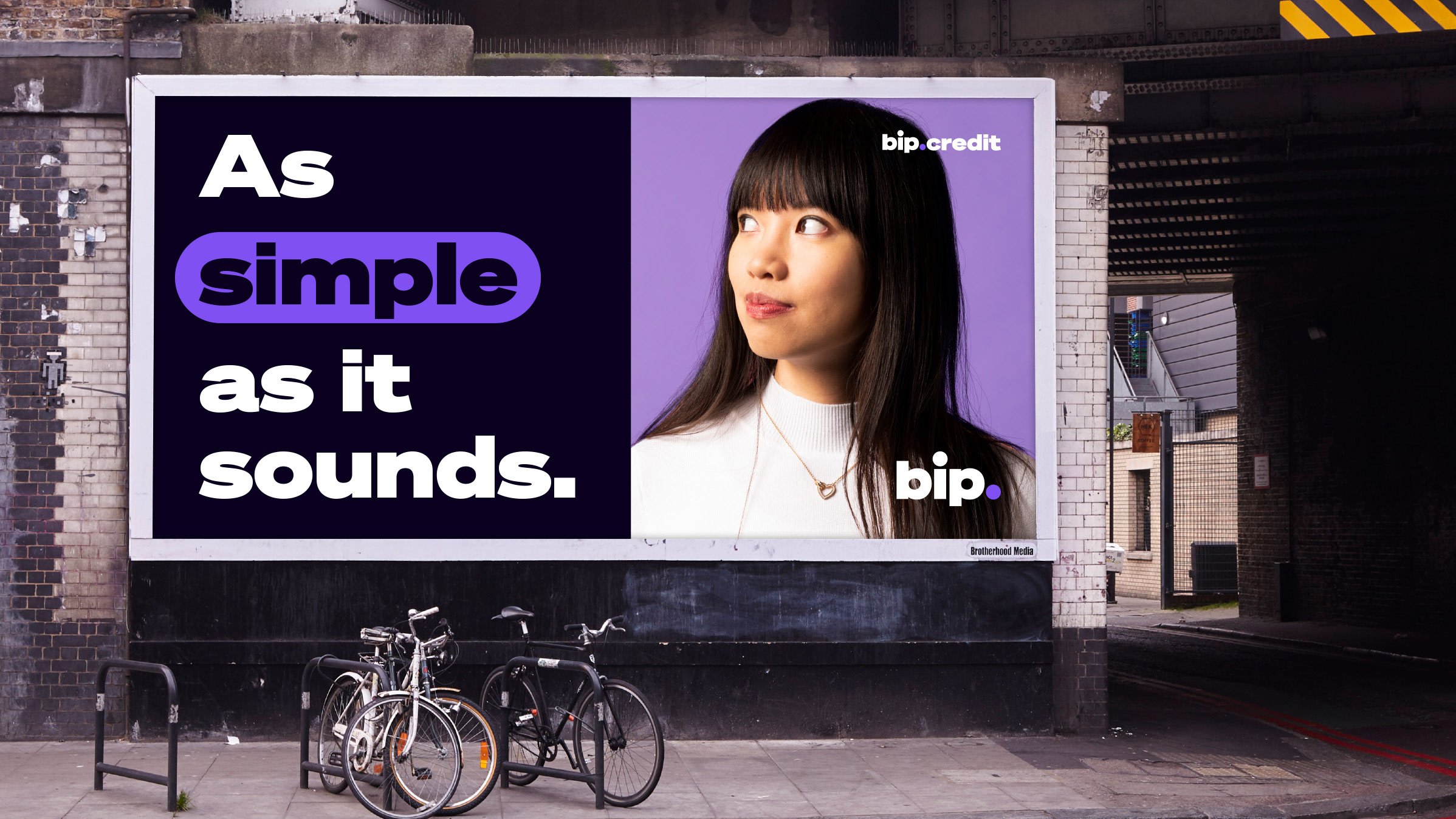 Billboard advertisement on a city wall showing a woman with long dark hair and a white top, with text 'As simple as it sounds.' on a purple and black background. The billboard promotes bip.credit with the logo and website at the bottom right.