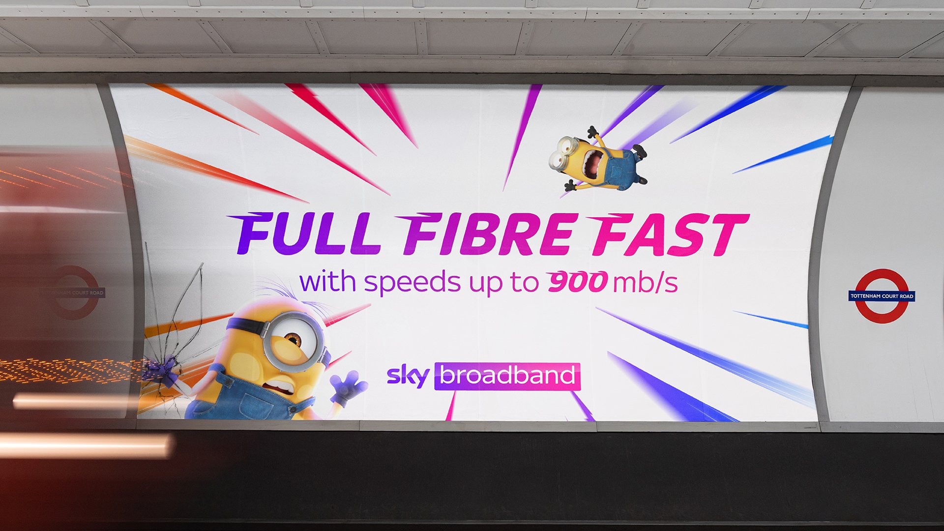 Billboard advertisement for Sky broadband featuring Minions characters, promoting full fiber fast internet with speeds up to 900 mb/s. The background has colorful streaks and Minions, with one breaking through the billboard and another flying above.
