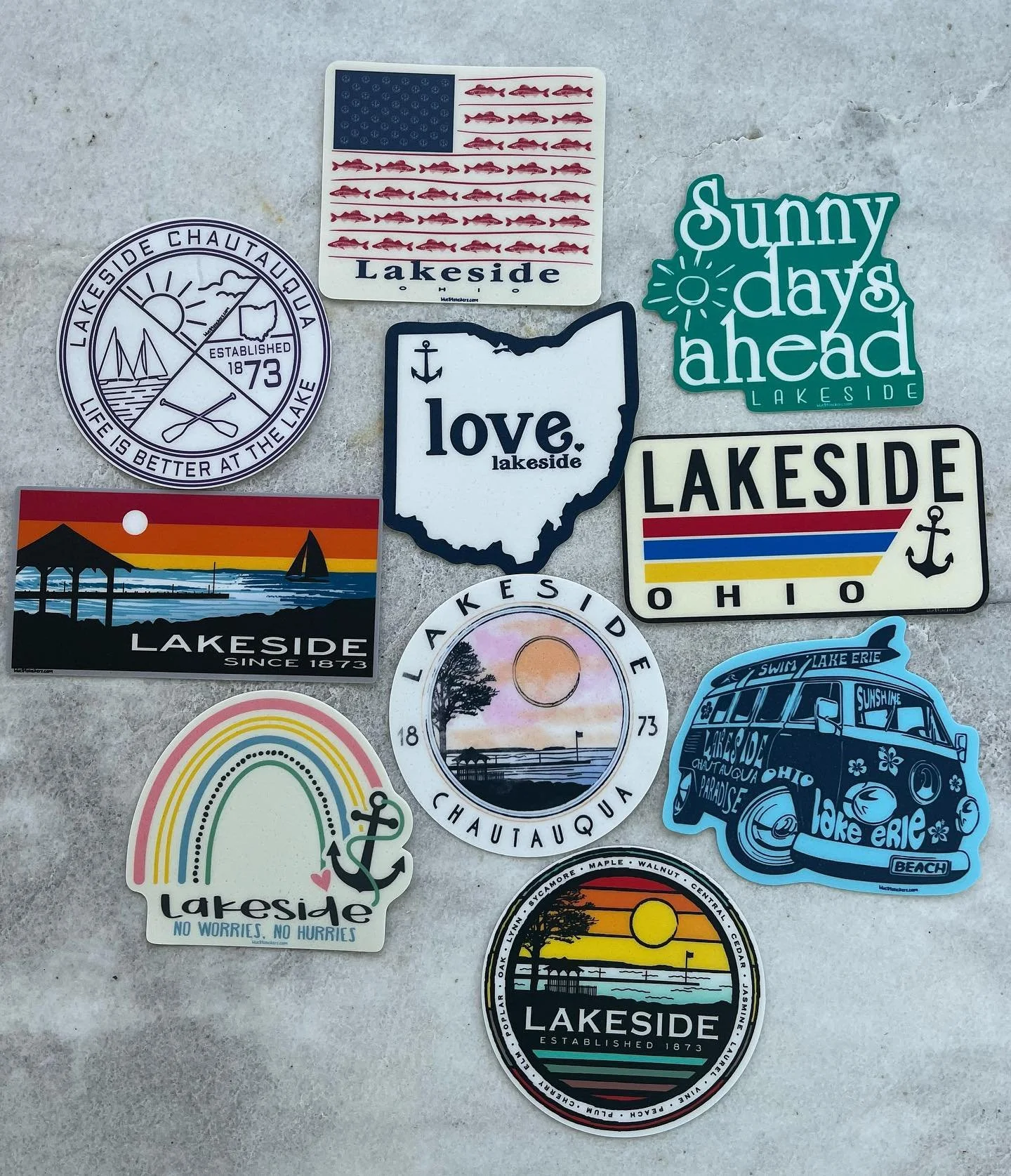 Collection of lakeside-themed stickers featuring American flags, sunsets, boats, rainbows, and phrases like "love lakeside," "sunny days ahead," and "no worries no hurries."
