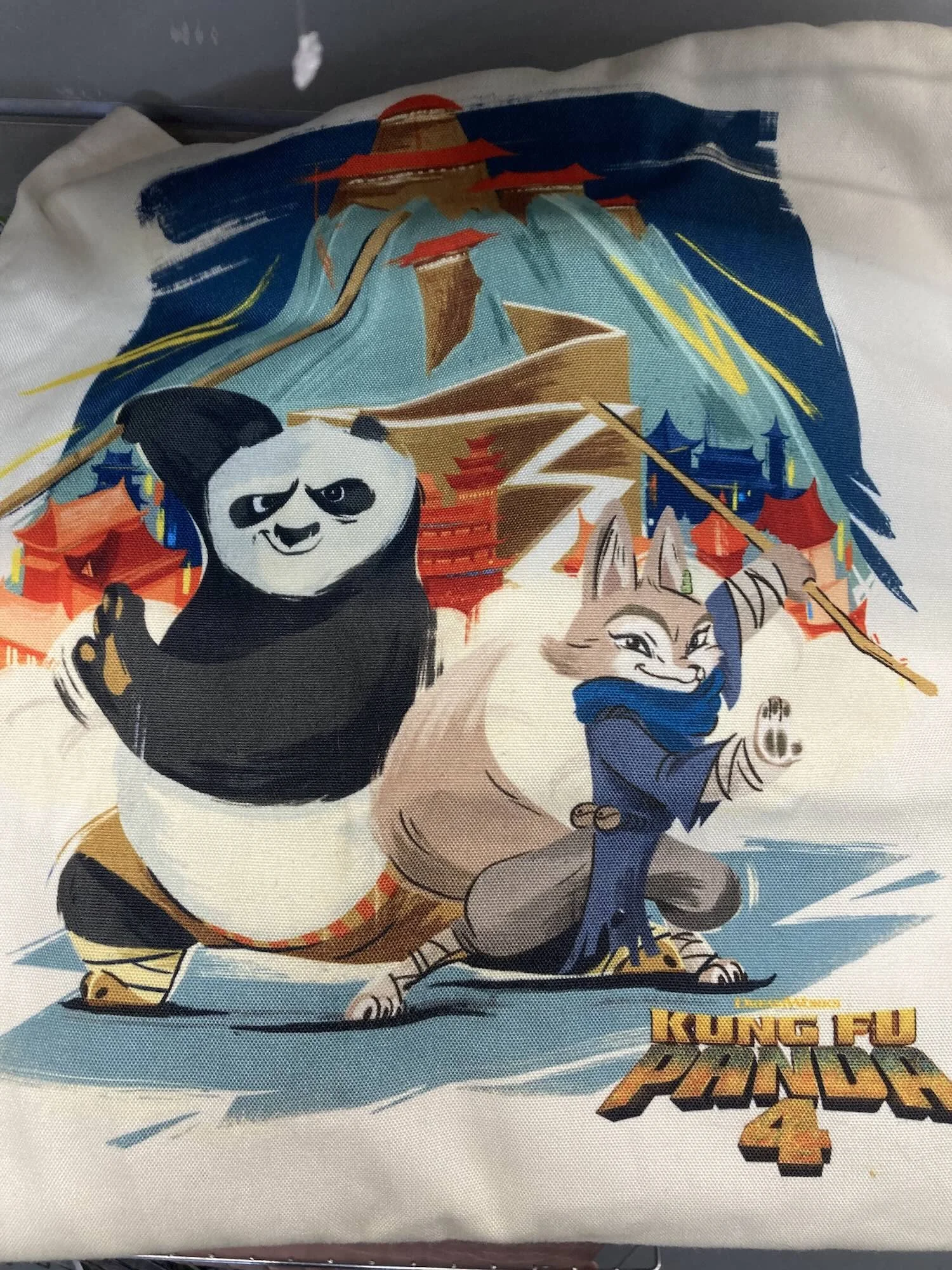 A tote bag with an Illustration from the movie Kung Fu Panda 4 with the panda and fox characters in front of a traditional Asian landscape.