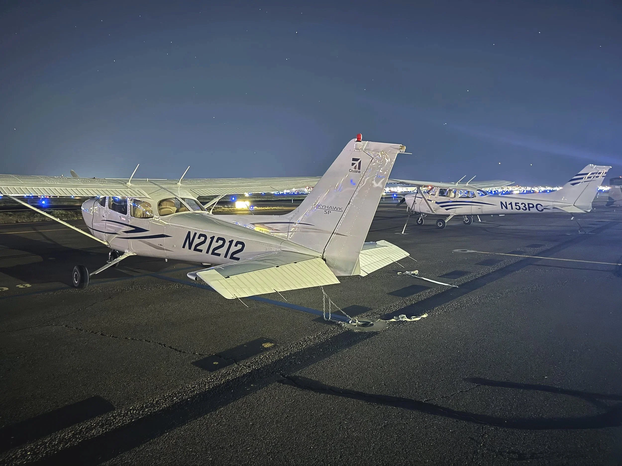 Nighttime view of small airplanes parked on an airstrip, illuminated by lights, with a clear sky above.