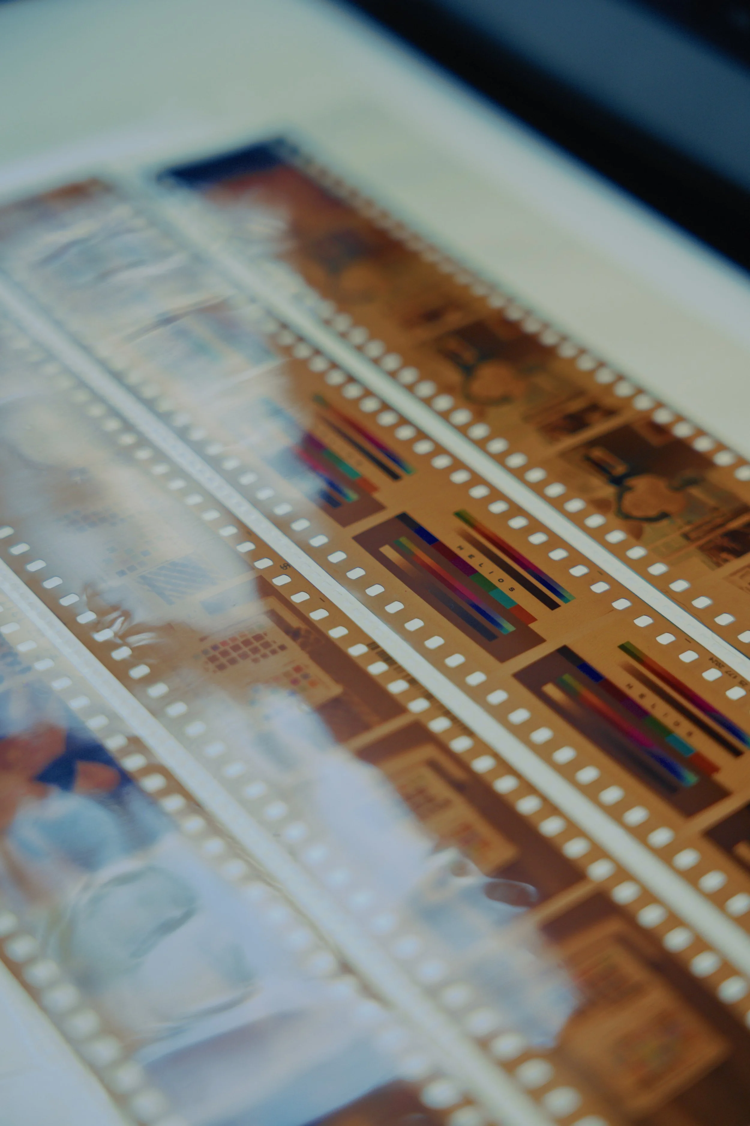 Close-up of photographic film strips with color test patterns and images, partially covered by a plastic cover.