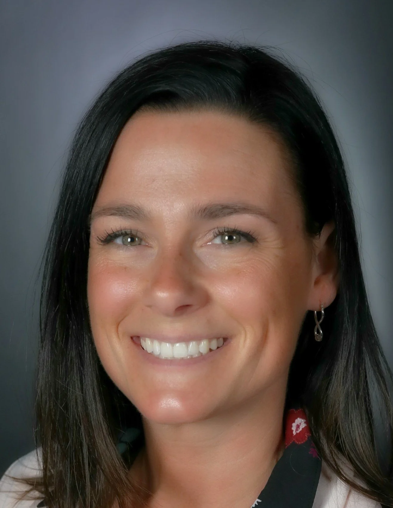 Close-up portrait of a smiling woman with dark hair, light skin, and earrings, wearing a black and red patterned scarf.