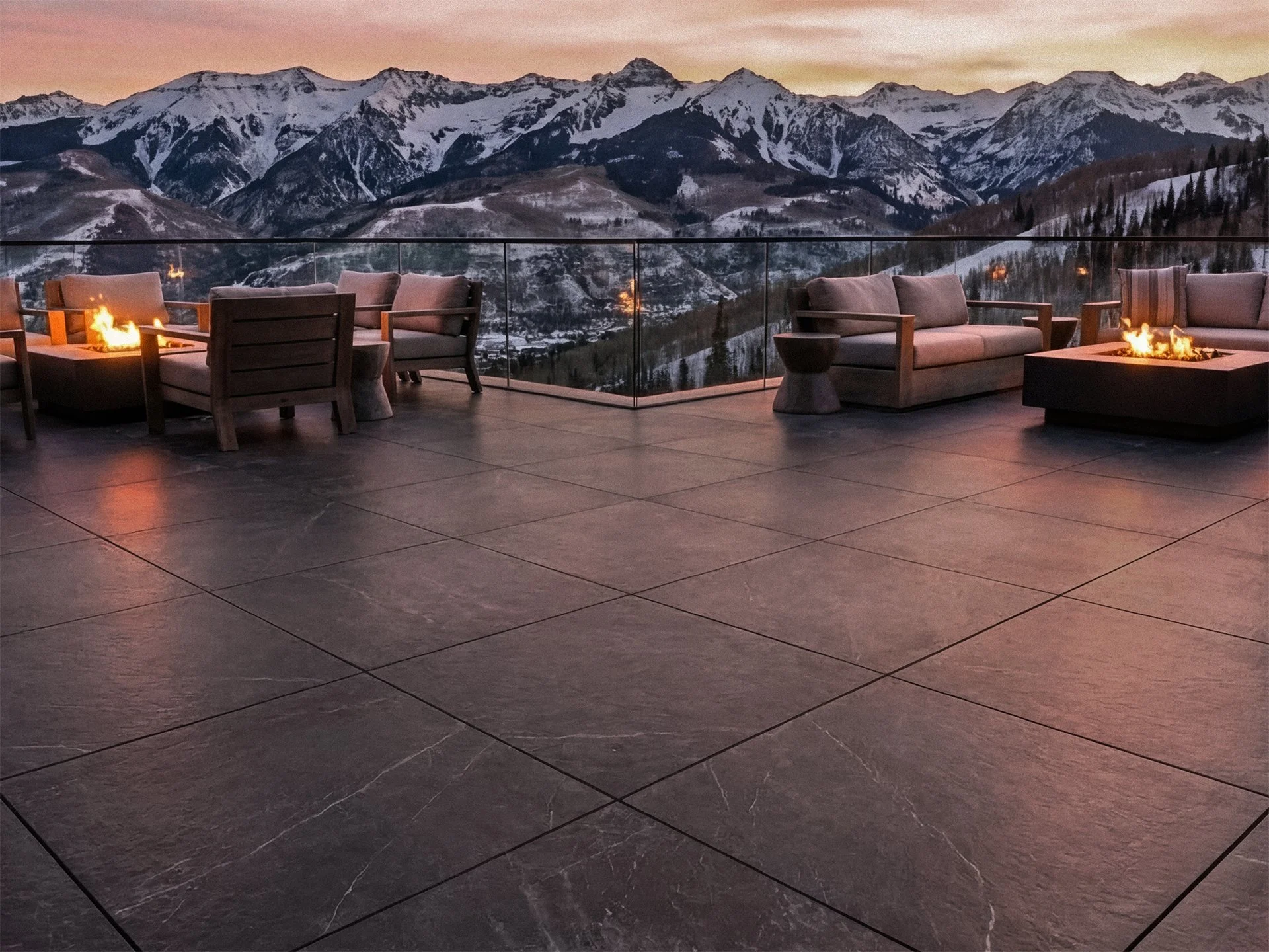 An outdoor patio with seating and fire pits overlooking snow-capped mountains at sunset.