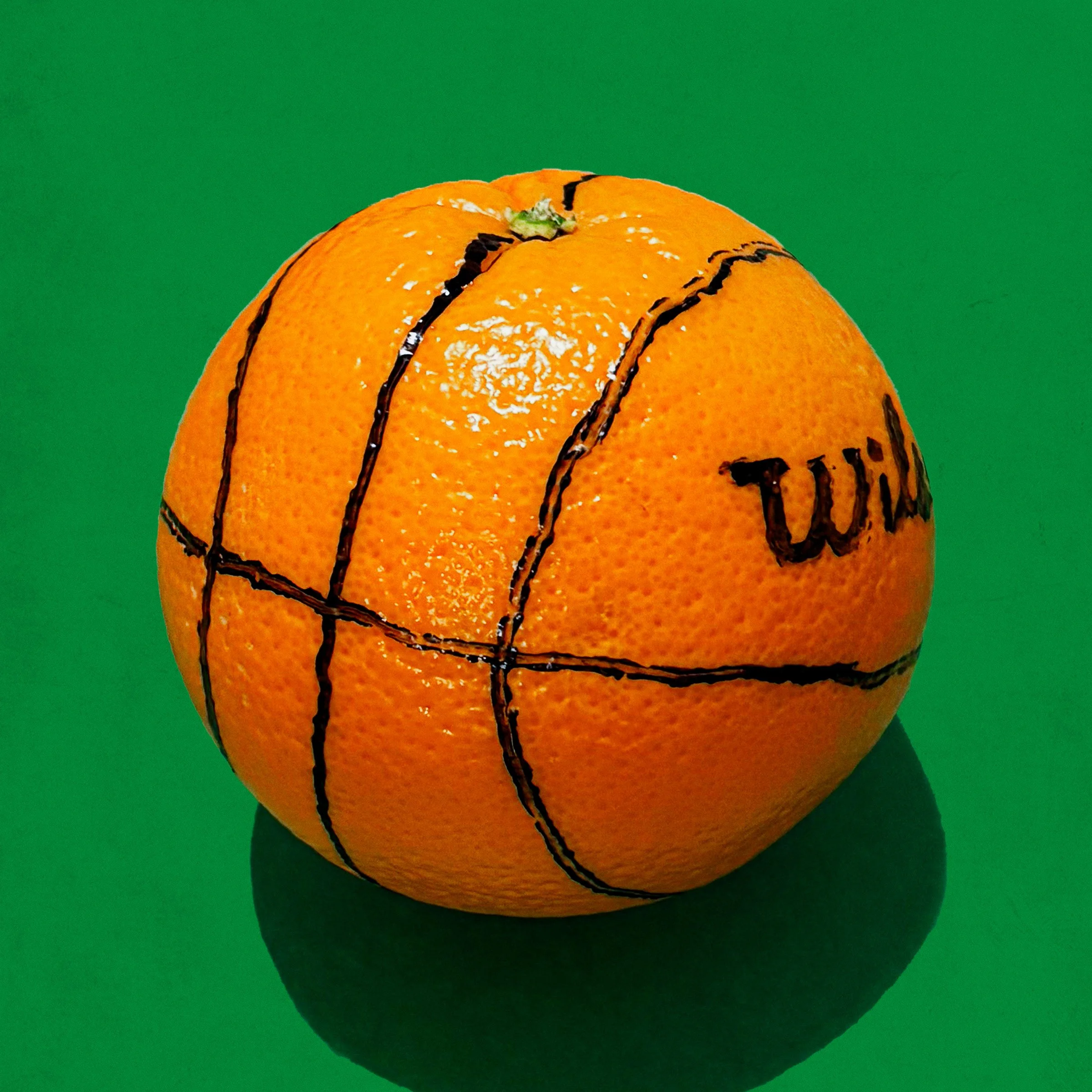 A photograph of an orange with basketball lines drawn on it in marker.