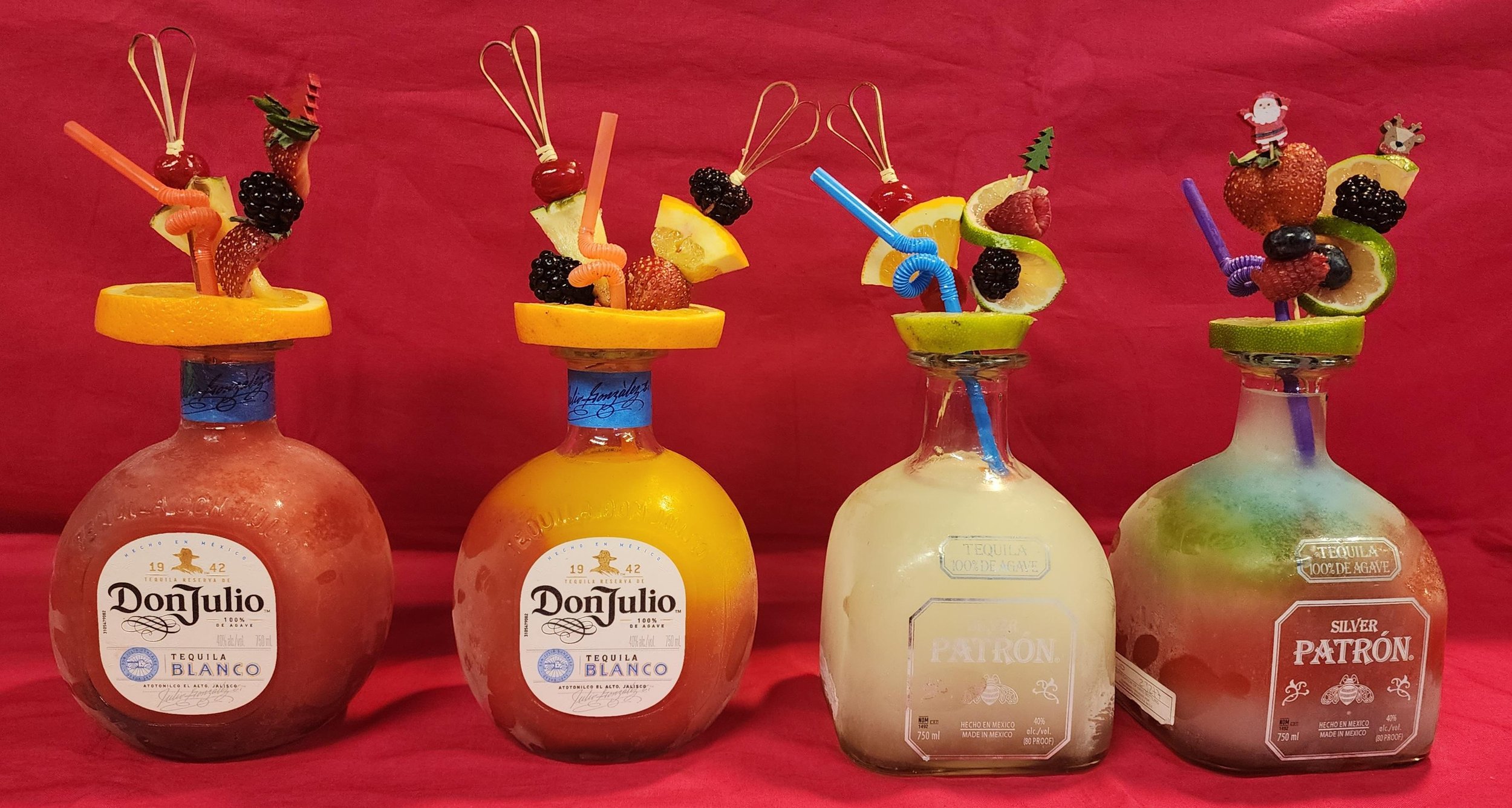 Four tequila bottles with fruit garnishes and colorful straws on their necks, set against a red background.