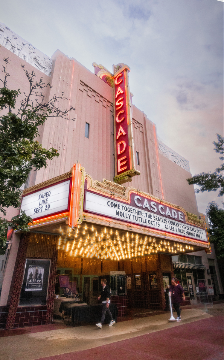 The front of the Cascade Theater with a vertical neon sign displaying the word 'CASCADE'. The marquee below shows upcoming performances, including Sahed live on September 29 and a Beatles concert experience featuring Molly Tuttle and AJ Lee & Blue Su