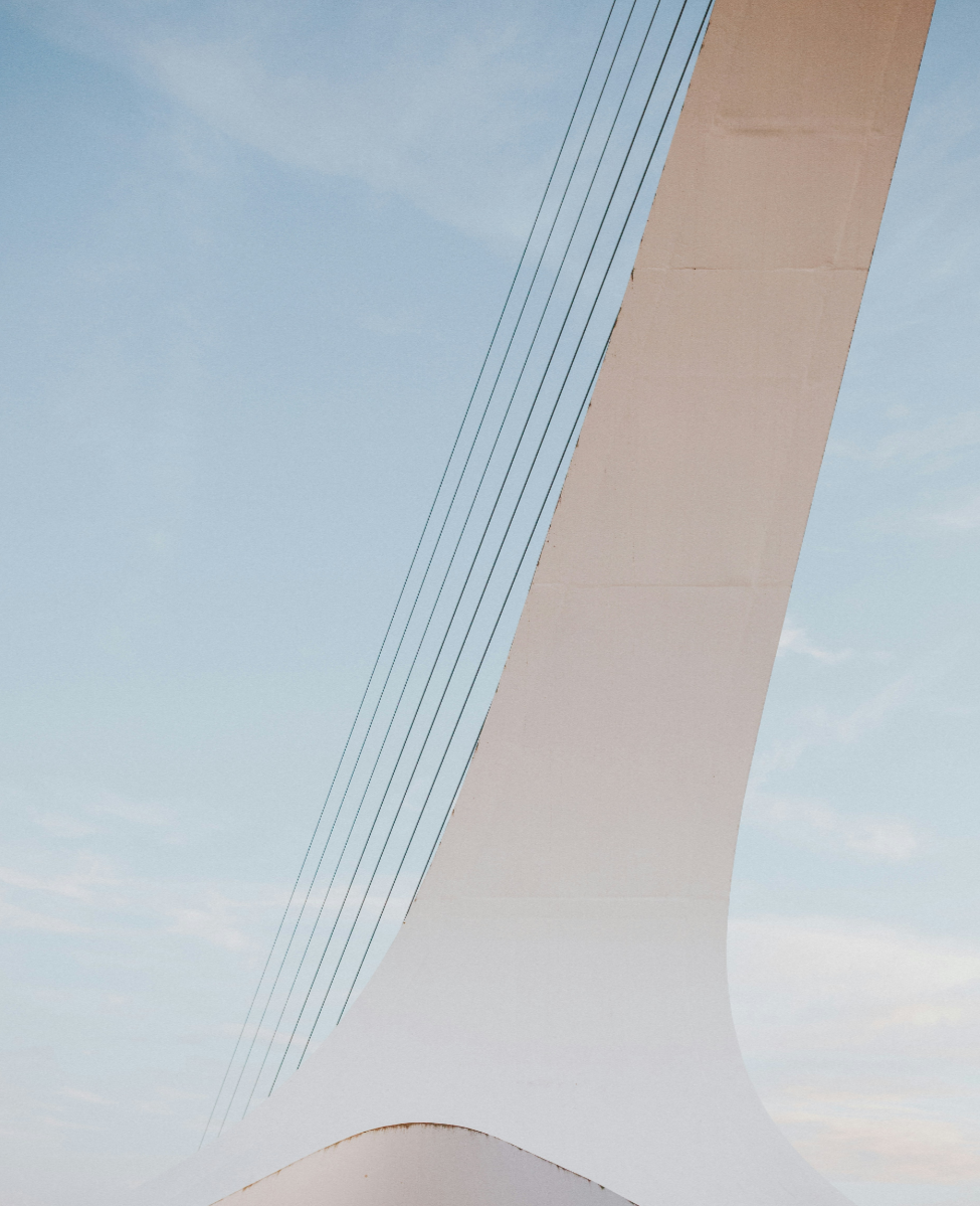 Close-up of a modern cable-stayed bridge pylon against a blue sky with light clouds.