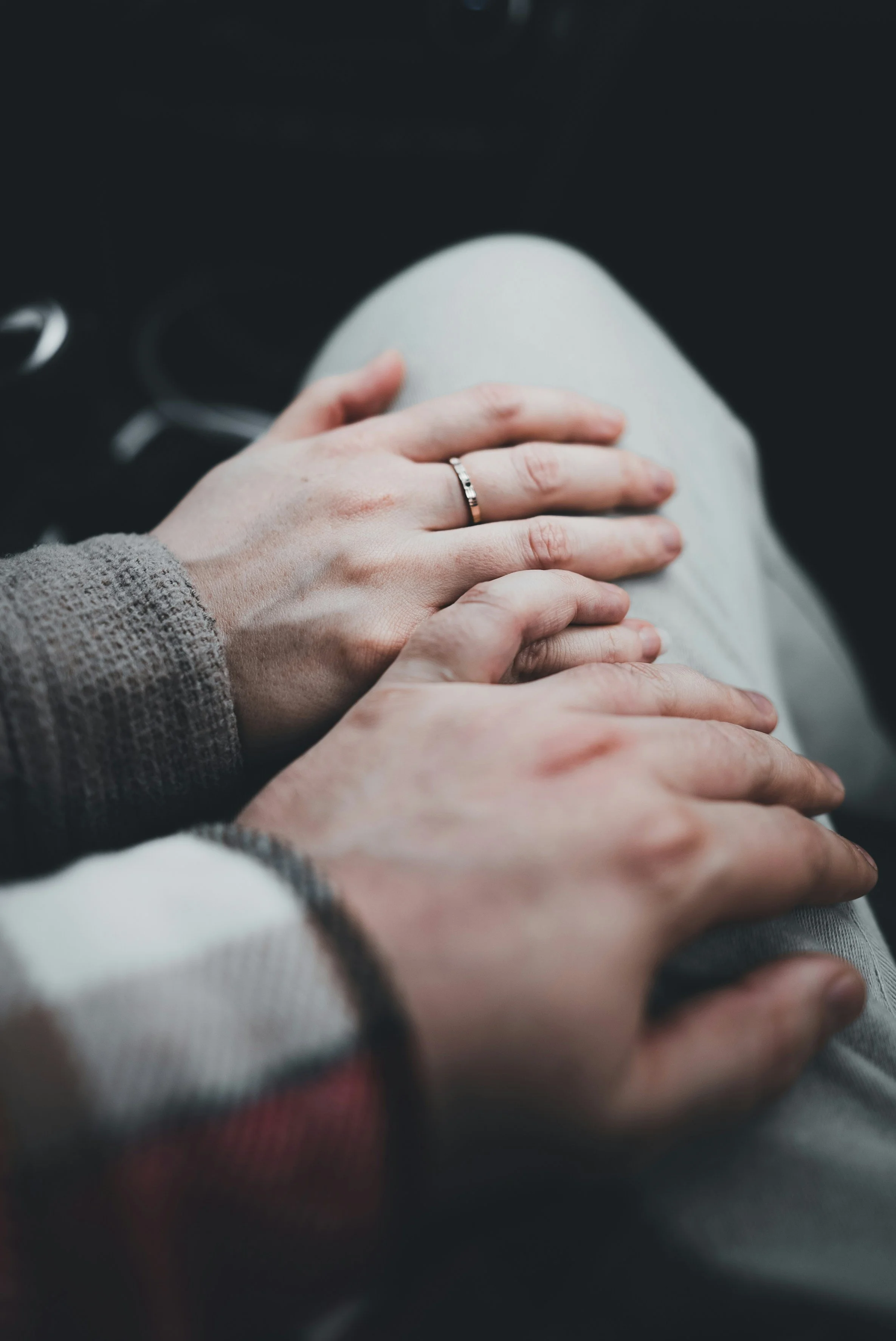 Close-up of a person's hand with a ring gently resting on another person's knee, wearing light-colored clothing, in an indoor setting.