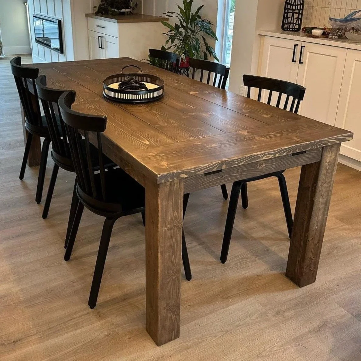 A classic 4 post dining table made of wood, with a medium brown finish, surrounded by black chairs in a dining room setting.