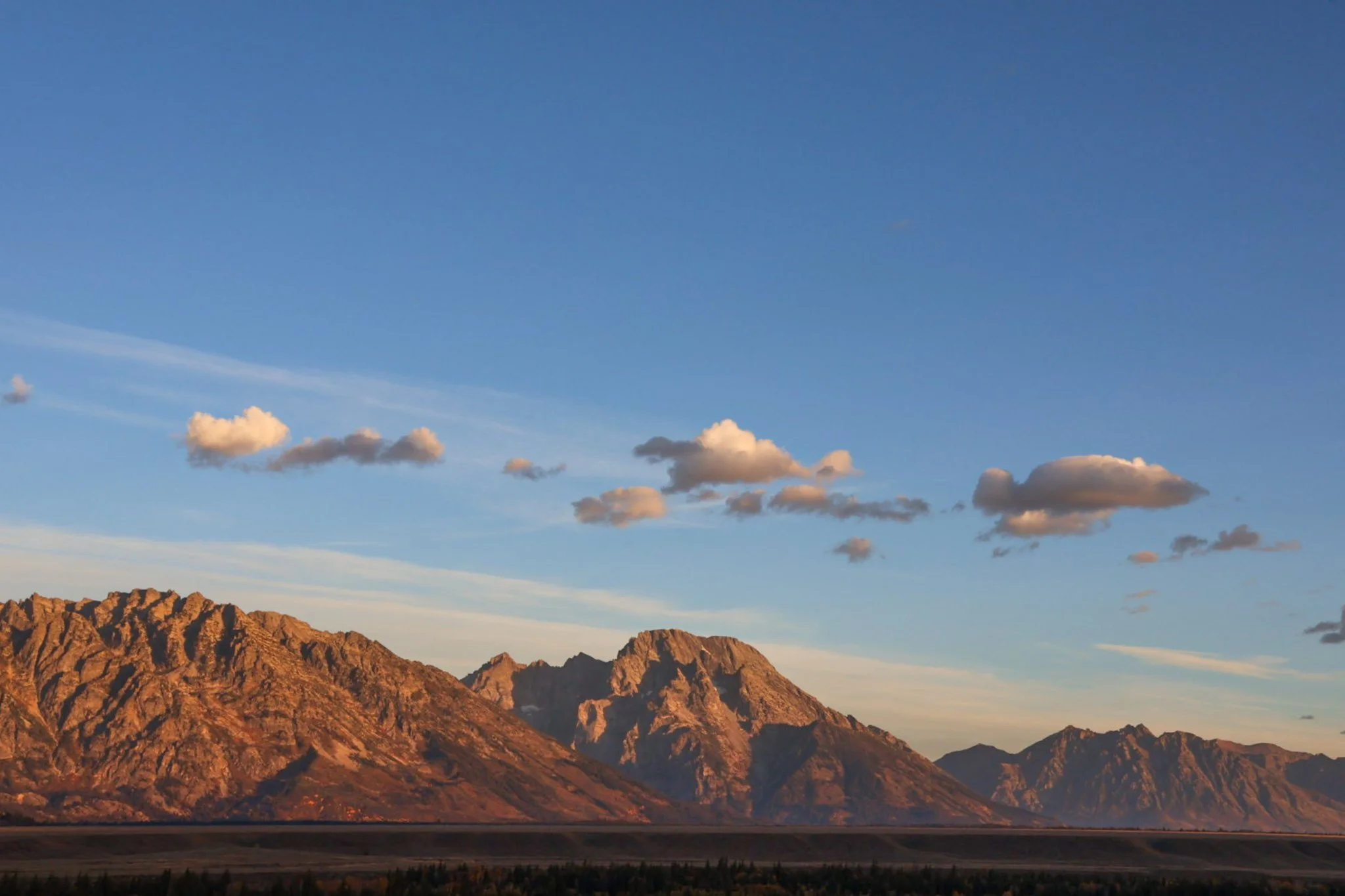 Mountain range at sunset with scattered clouds in a blue sky.