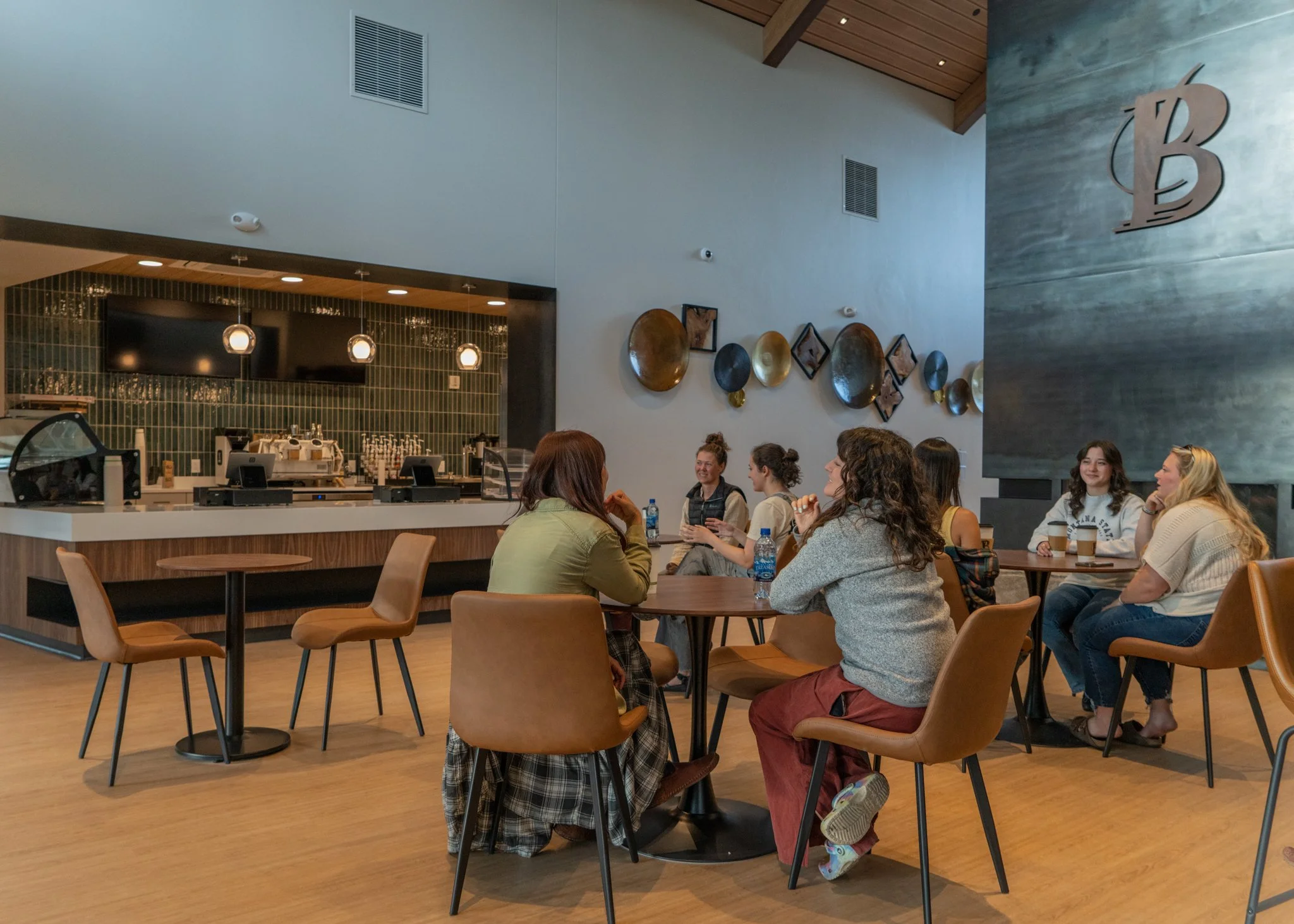 A group of women sitting around tables chatting in a coffee shop with a modern interior.