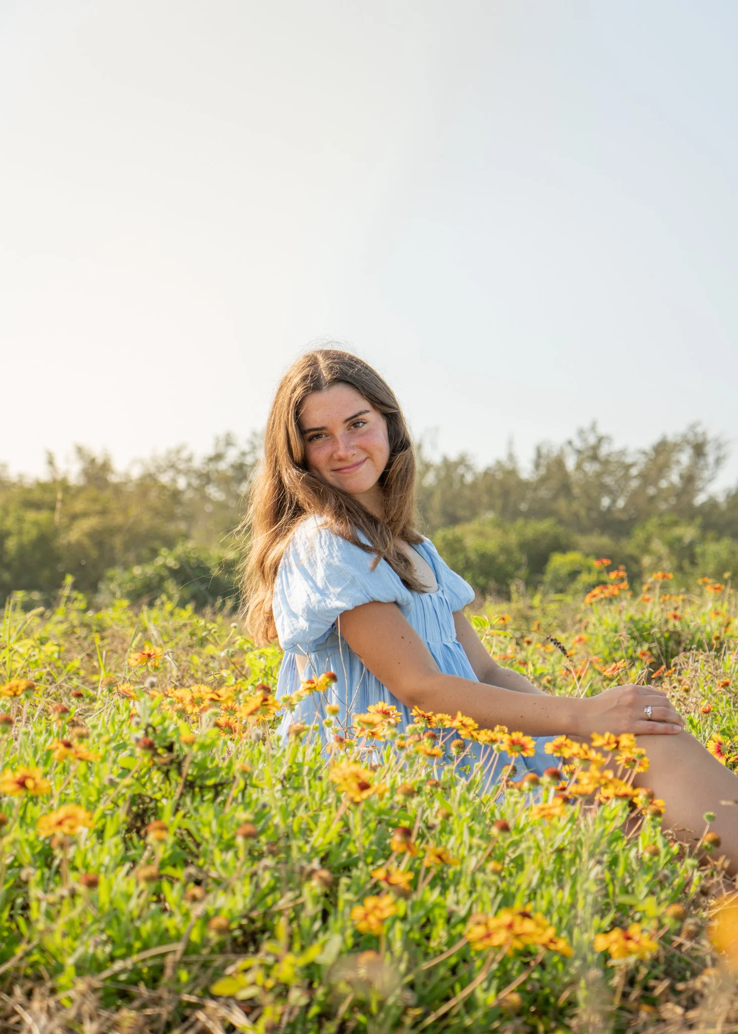 Young woman sitting in field of yellow and orange flowers during sunlight.
