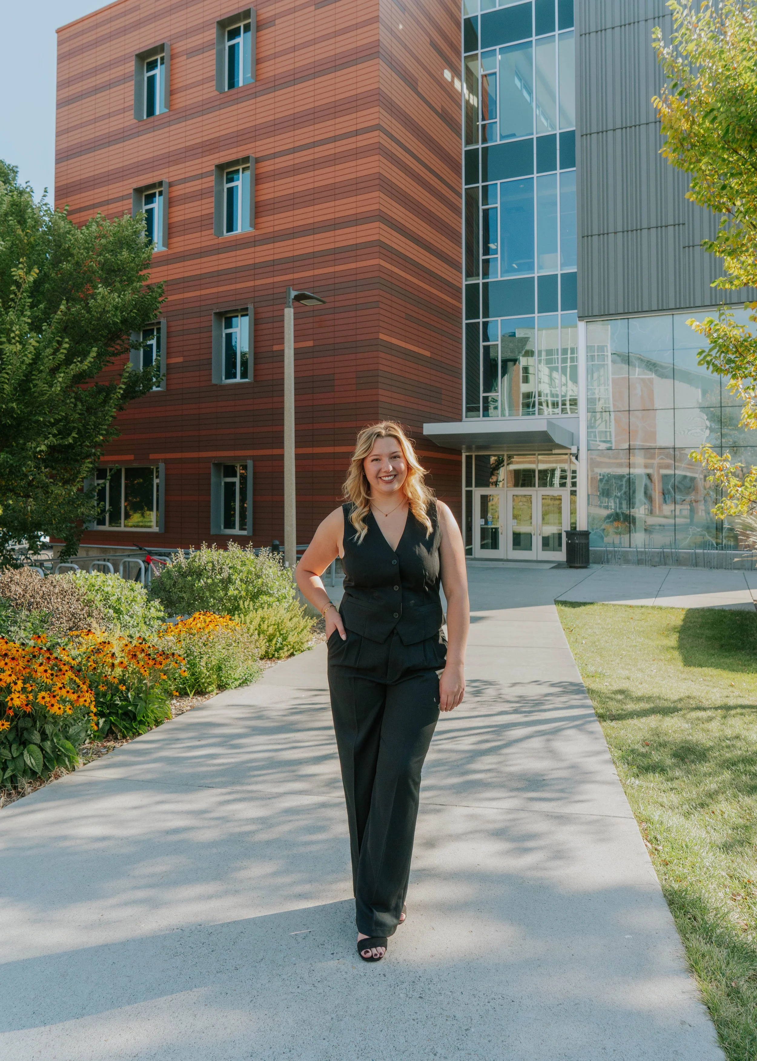 Smiling woman in black business attire walking on sidewalk outside modern office building