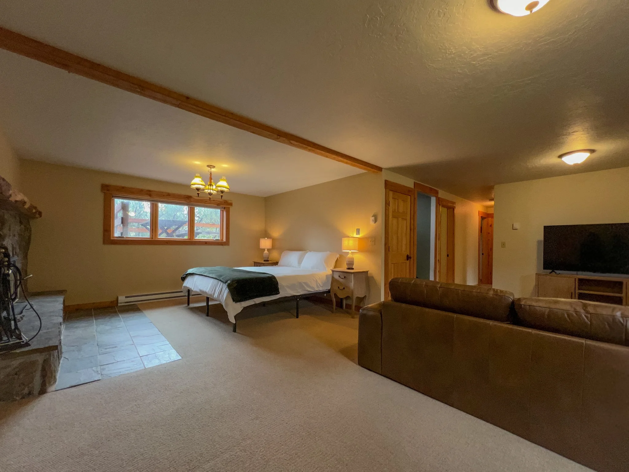 Interior of a cozy bedroom with a large bed, nightstands, lamps, a leather sofa, a fireplace, and a flat-screen TV.