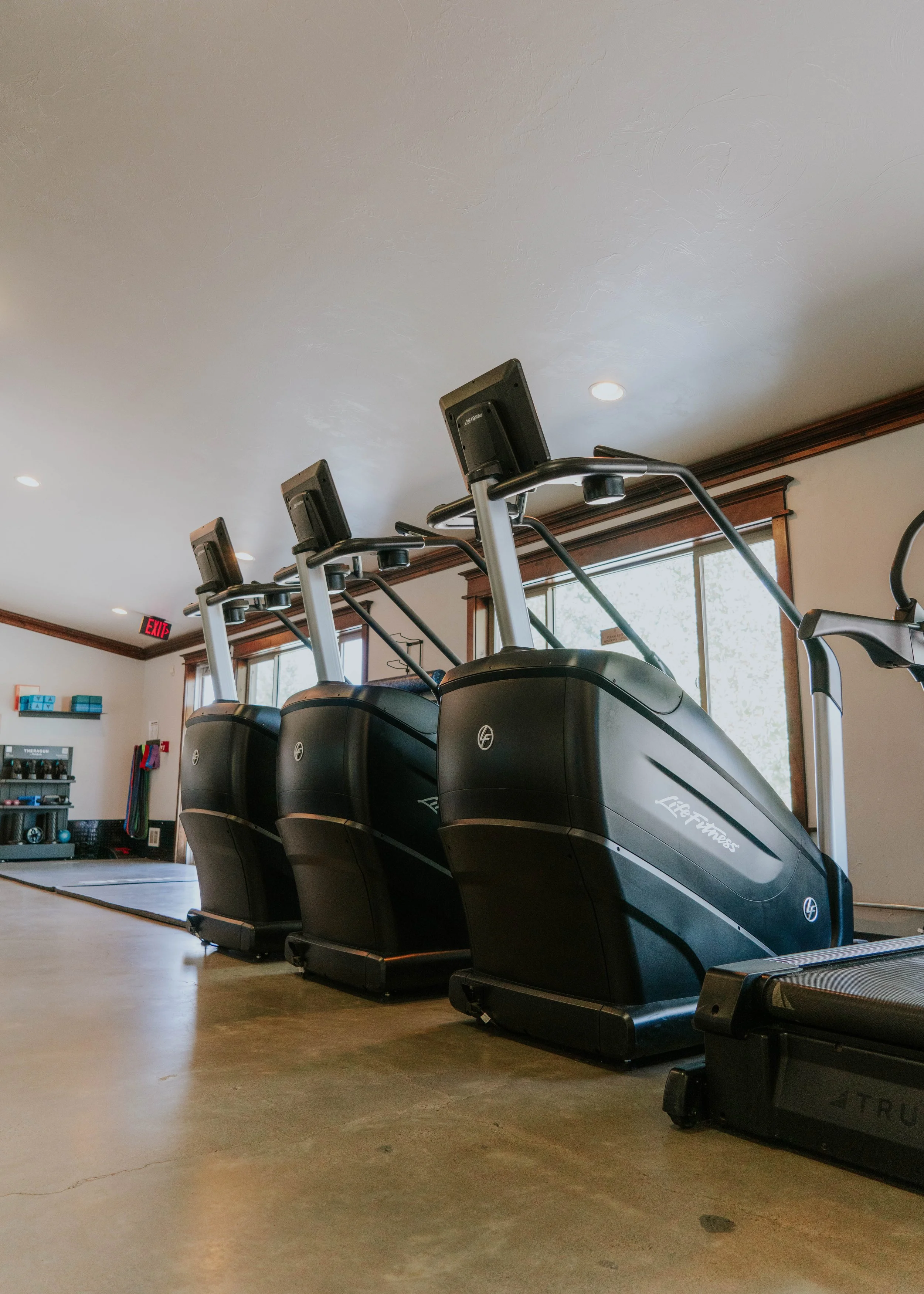 Three Life Fitness elliptical machines in a room with wooden trim and windows