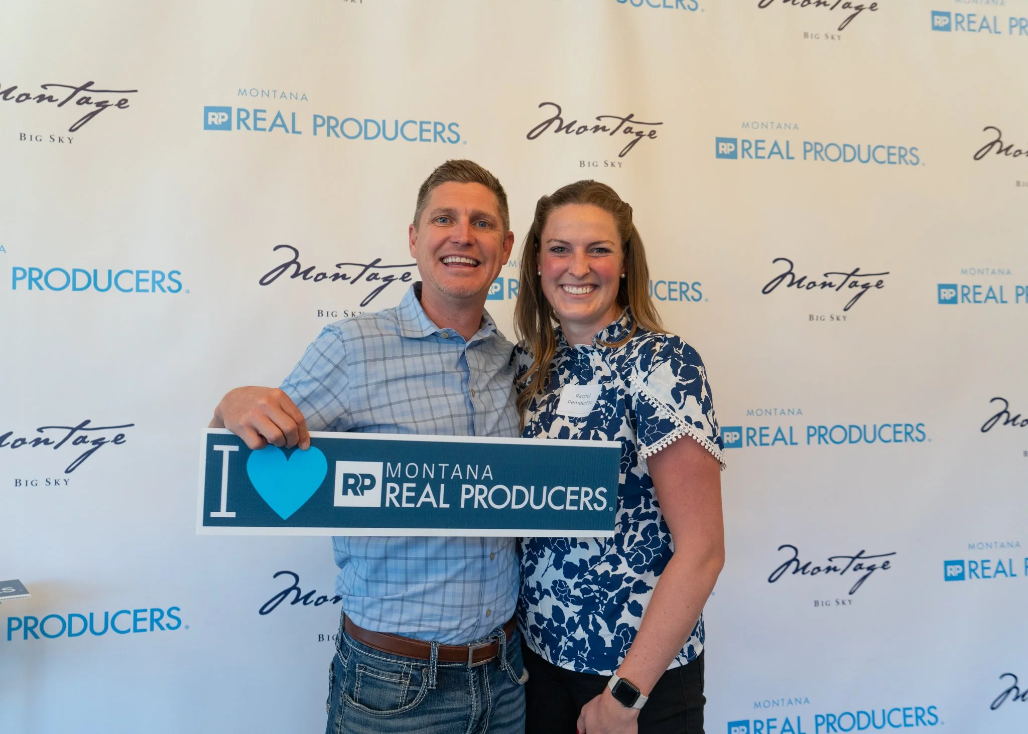 Two smiling people, a man and a woman, holding a sign that reads "I ❤️ RP Montana Real Producers," standing in front of a backdrop with logos for Montana Real Producers, Montage Big Sky.