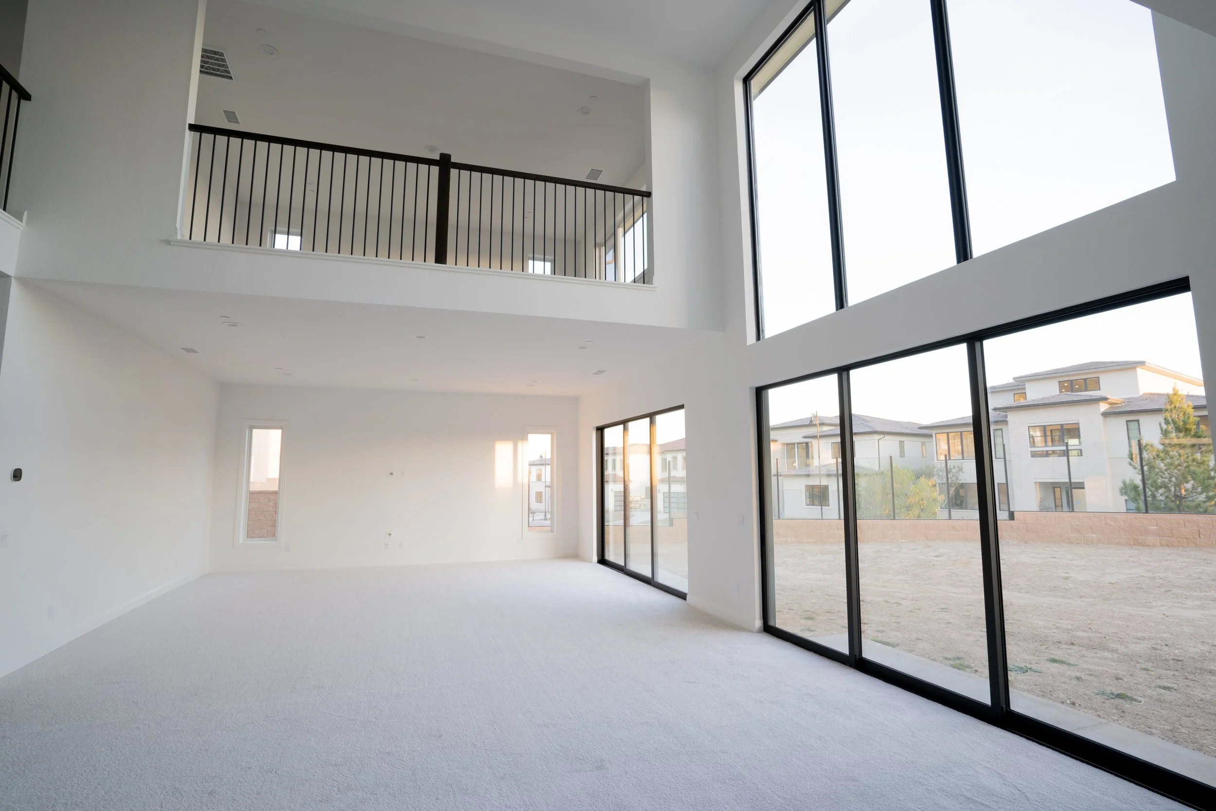 Interior of a modern home with large floor-to-ceiling windows, white walls, and a high ceiling.