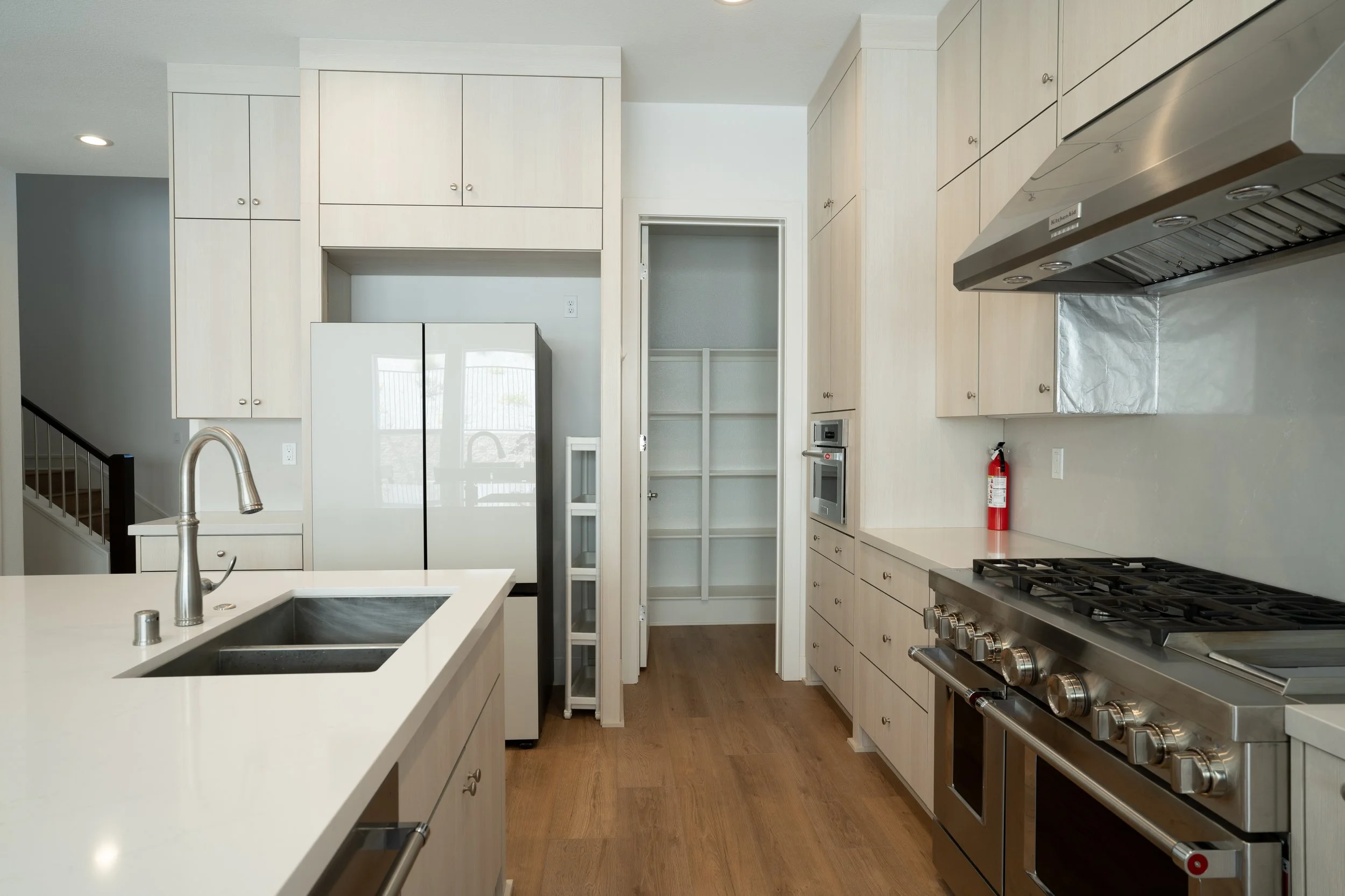 Modern kitchen with white cabinets, stainless steel appliances, a gas stove, and a refrigerator, with a center island and hardwood floors.