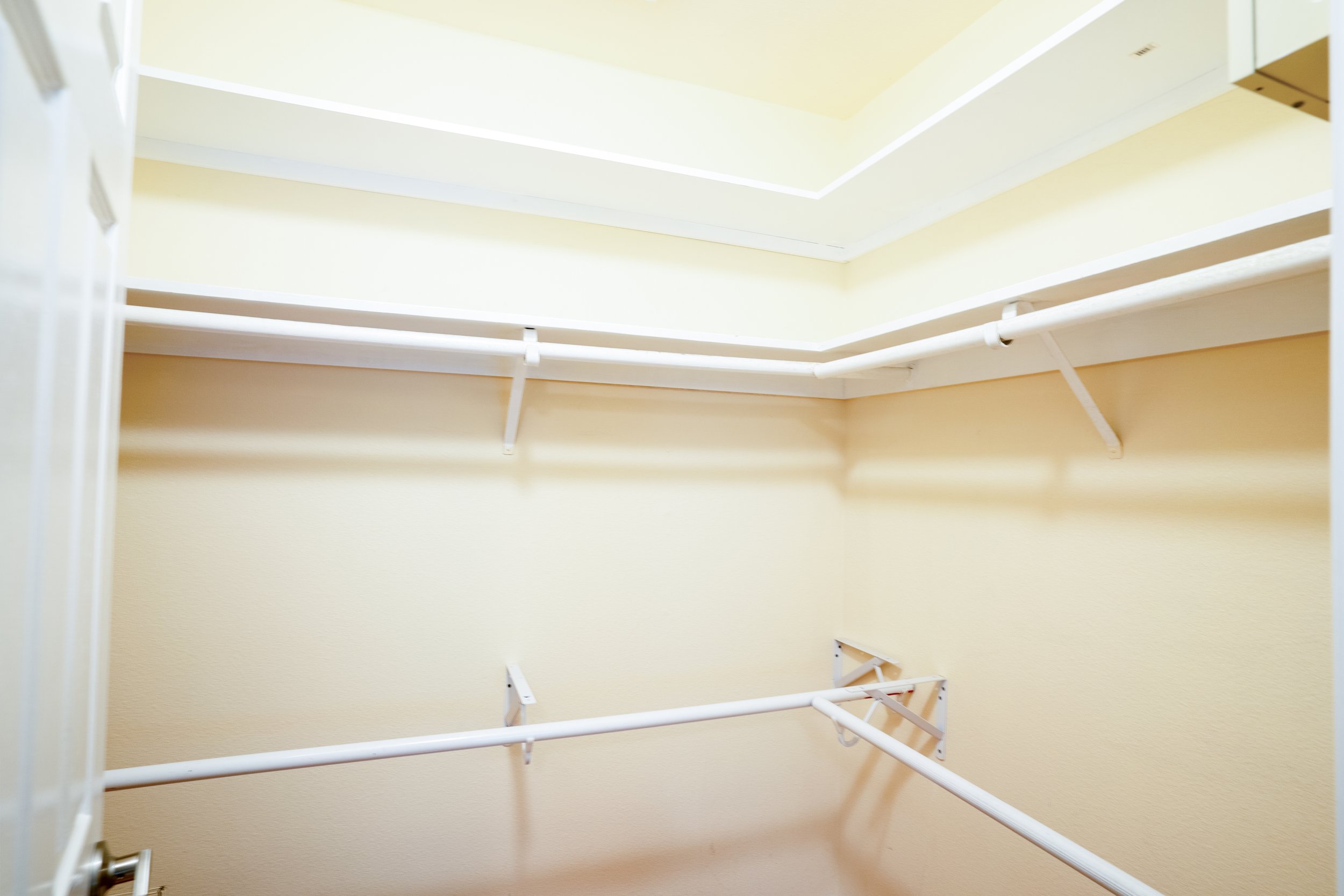 Empty walk-in closet with multiple white wire shelves and hanging rods, painted light yellow walls.