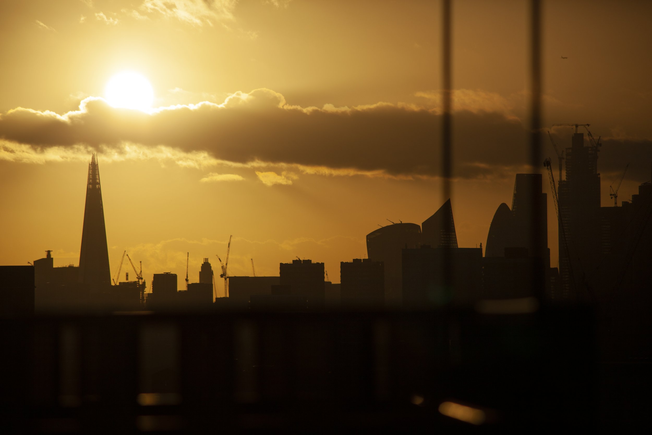 Sunset over the London skyline with recognizable skyscrapers, including The Shard, silhouetted against a golden sky with clouds.