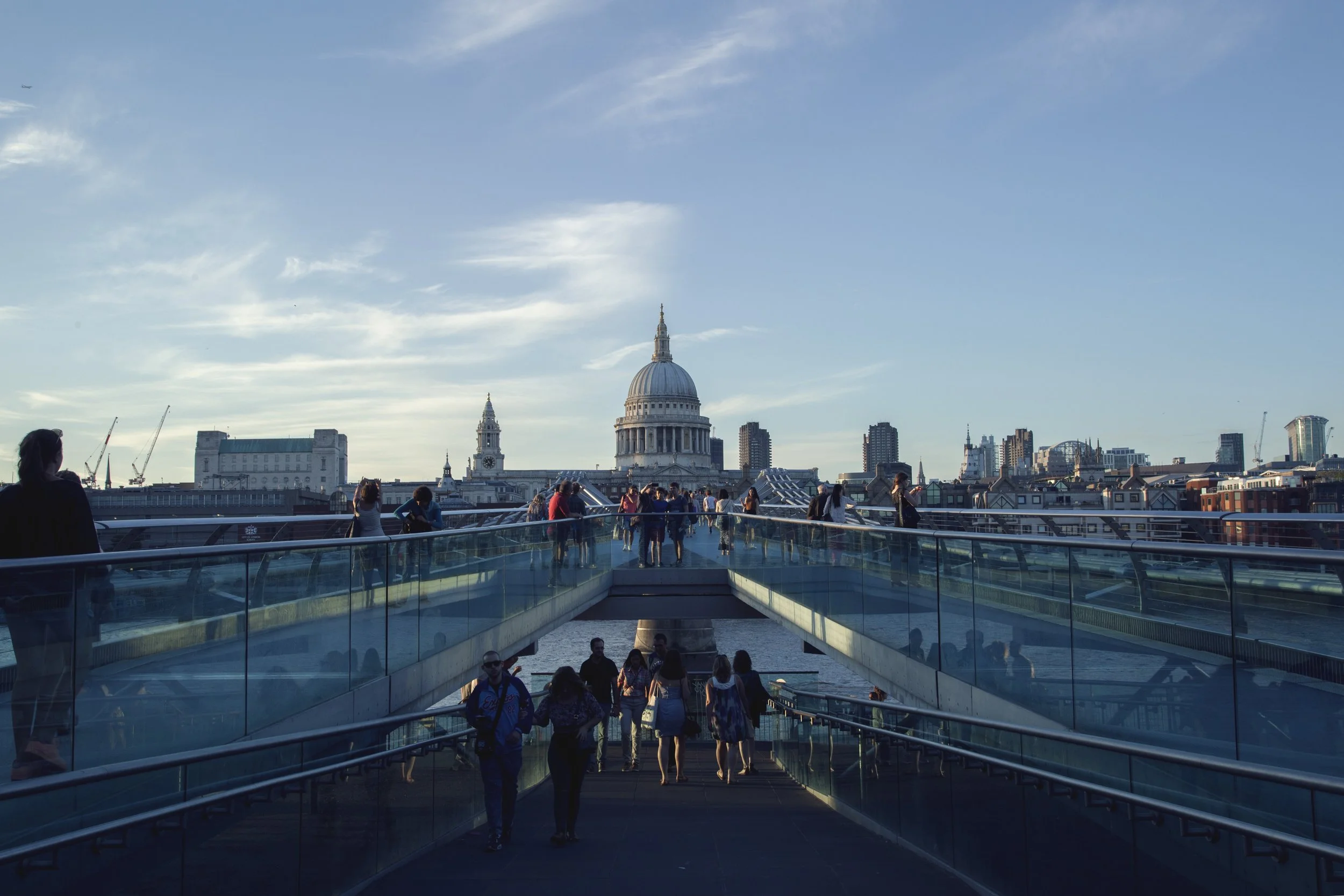People walking on the Millennium Bridge in London with St. Paul's Cathedral in the background during daylight.