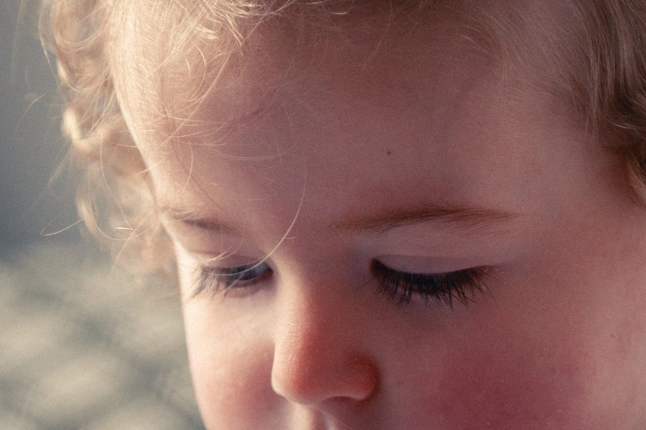 Close-up of a young child's face with eyes closed, showing curly blonde hair and long eyelashes.