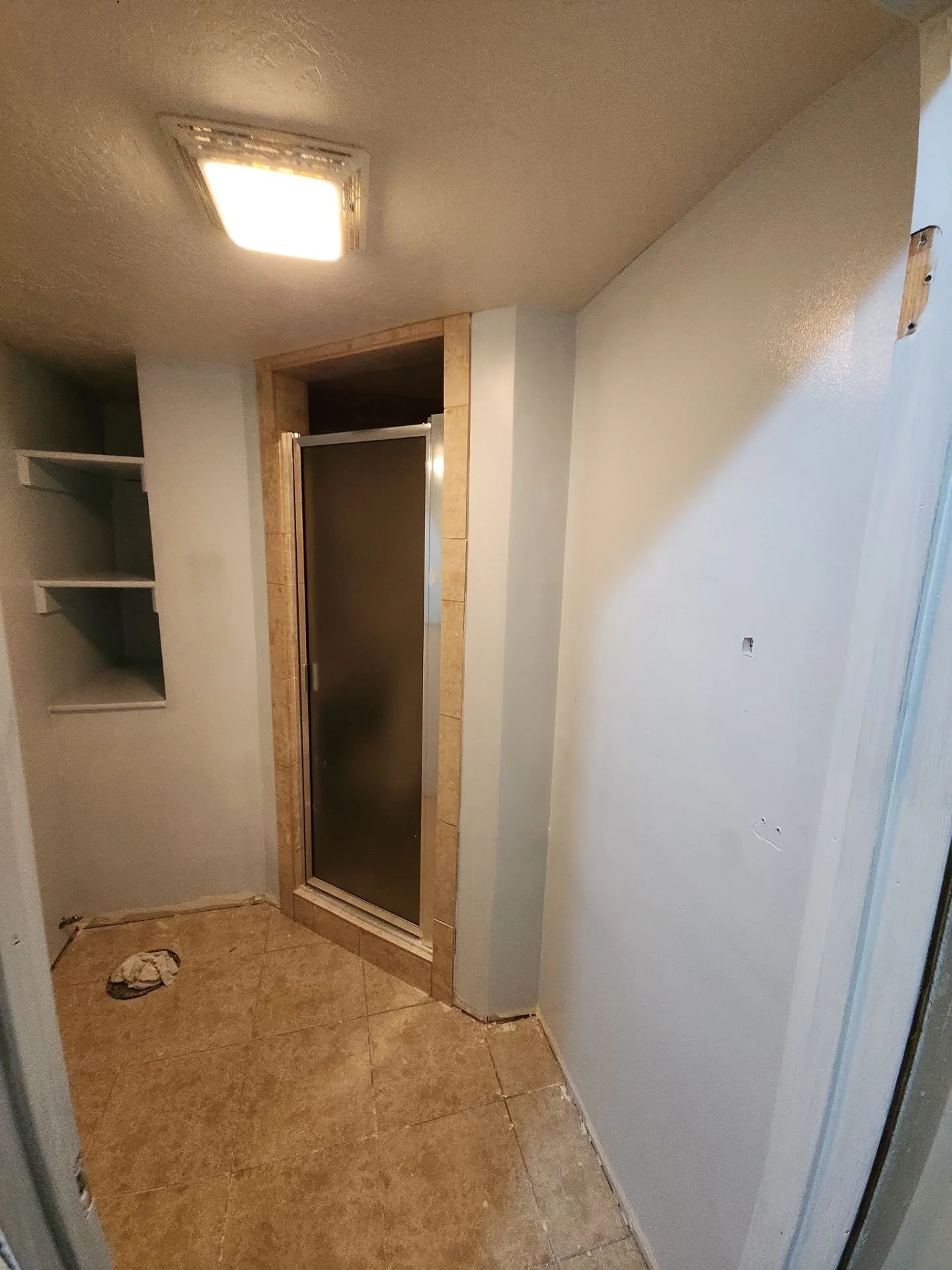 Small bathroom with a tiled shower enclosure, unfinished walls, and open shelving on the left.