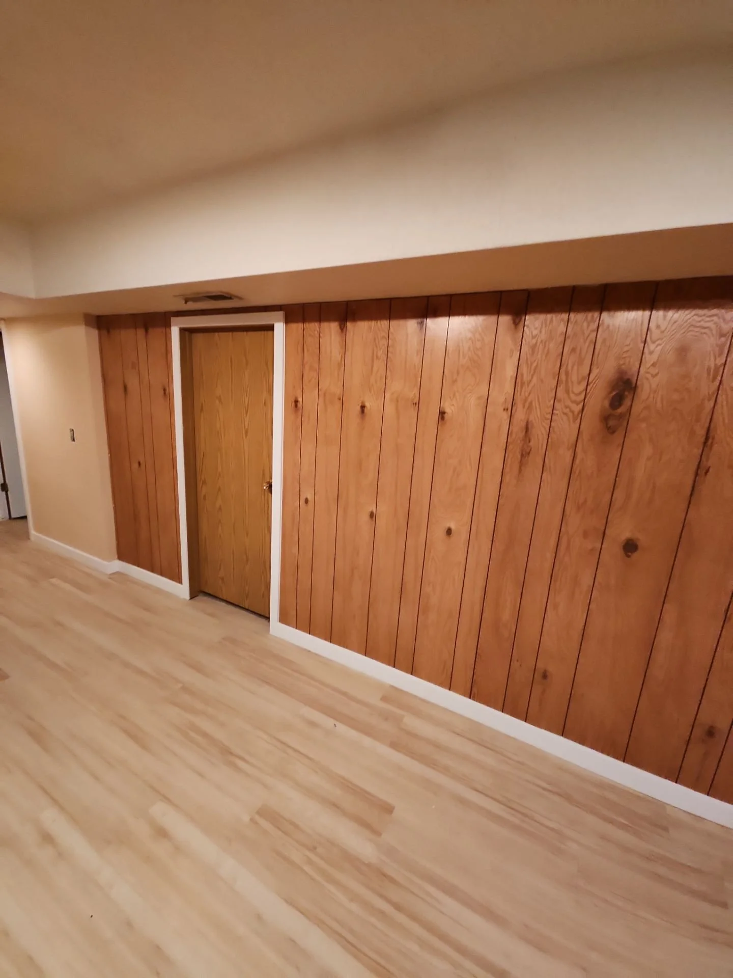 Room with wood-paneled wall and wooden floor, featuring a closed door with a white frame.