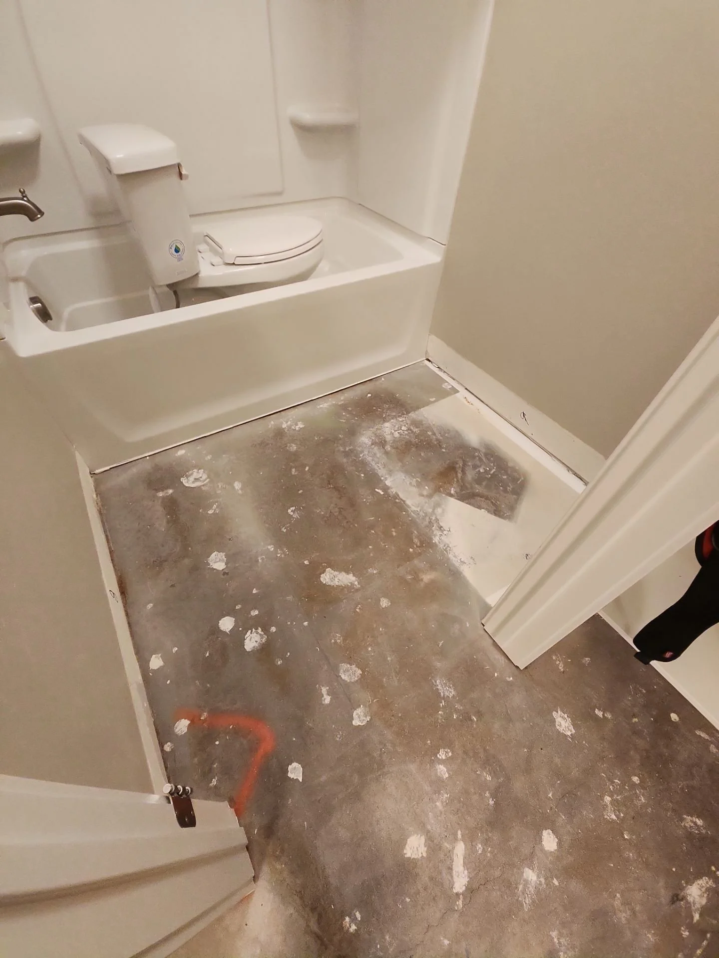 Bathroom with a bathtub, a toilet with a sink, and a partially renovated floor showing exposed subfloor and construction materials.