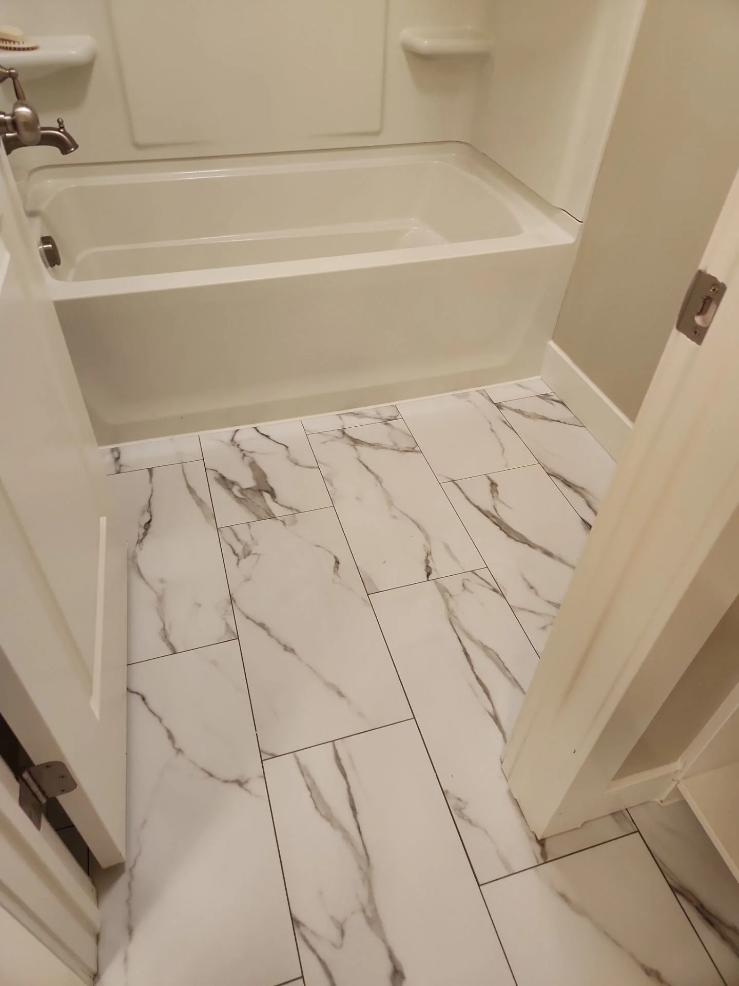 A bathroom with marble-patterned floor tiles, a white bathtub with a curved edge, and a wall-mounted faucet.