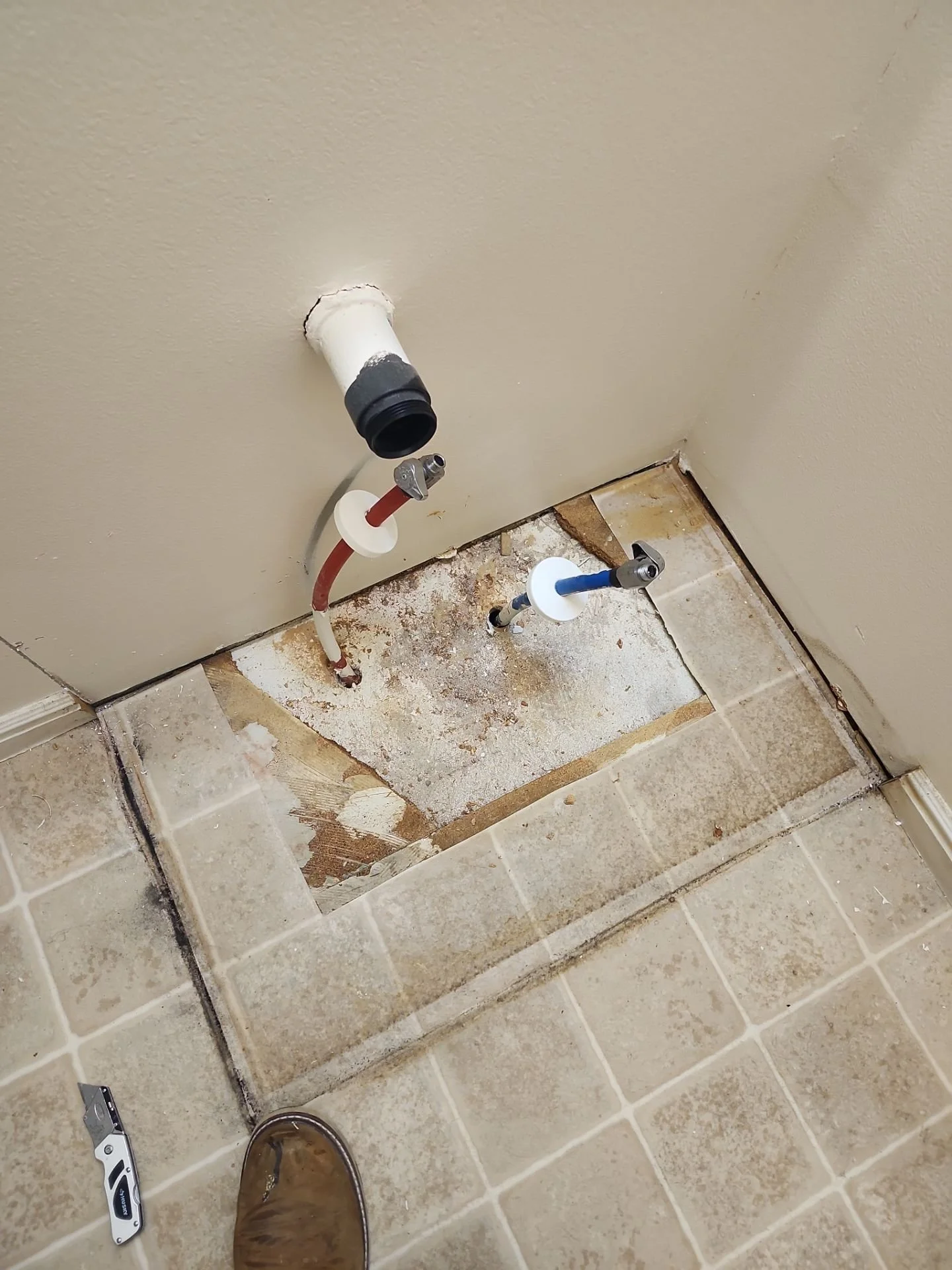 Photo of a bathroom or laundry room floor with the removed plumbing and drain area, showing exposed pipes and unfinished flooring.