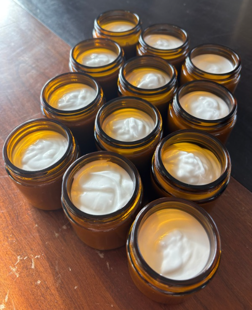Multiple small amber glass jars filled with a white cream or lotion, arranged on a wooden surface.