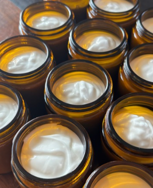 Multiple amber glass jars filled with a white cream or tallow arranged on a wooden surface.