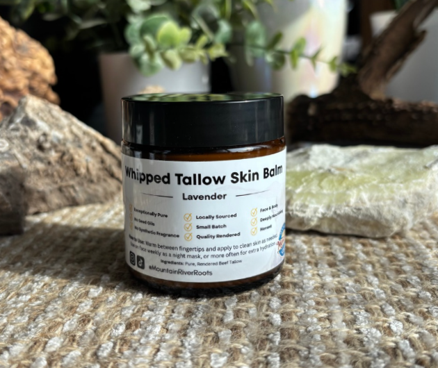 Scenic landscape with a large body of water in the foreground, rolling grassy hills, and mountain range in the background under a cloudy sky.