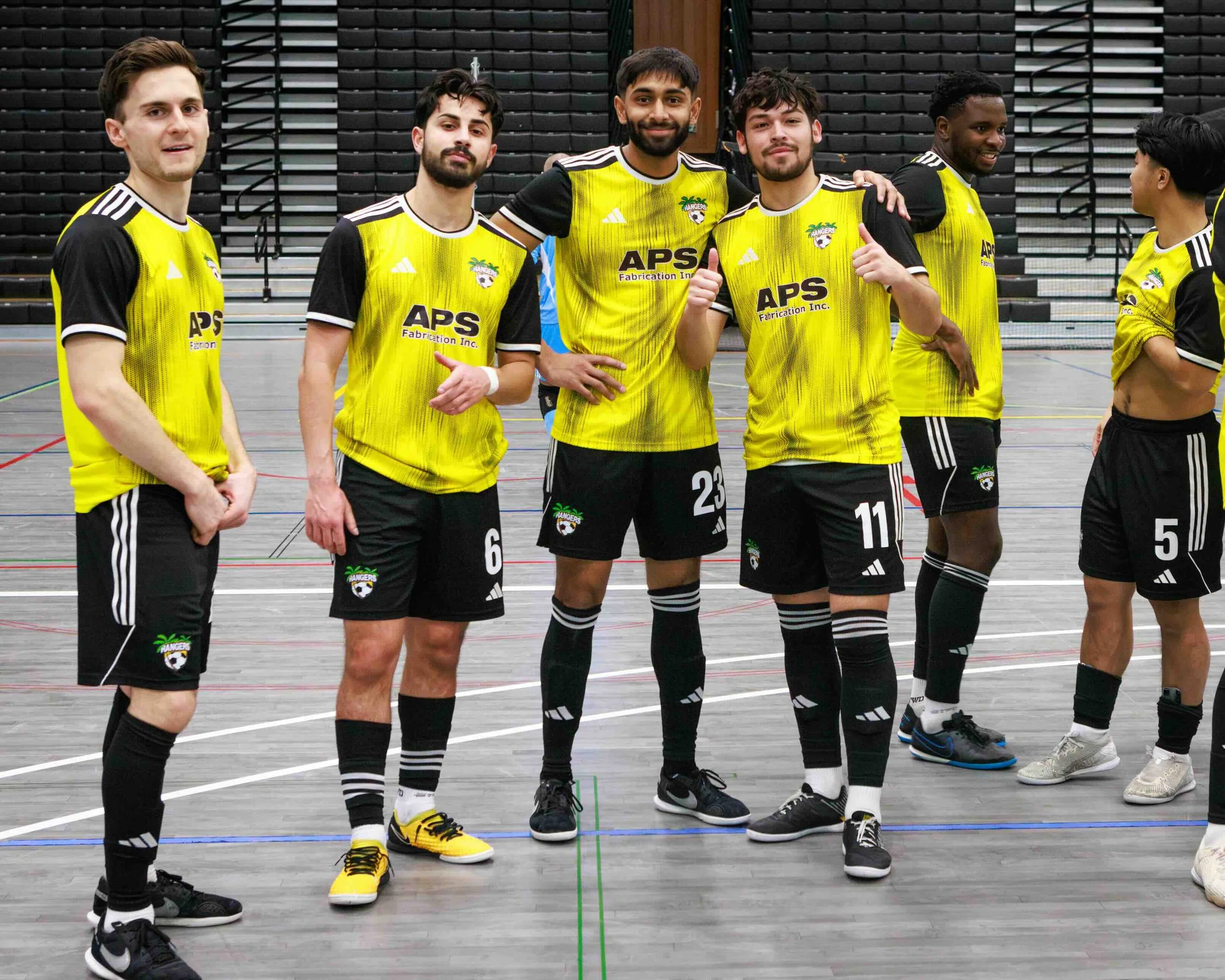 Group of six male indoor soccer players in yellow and black team uniforms standing on a court, some smiling and posing for the photo.