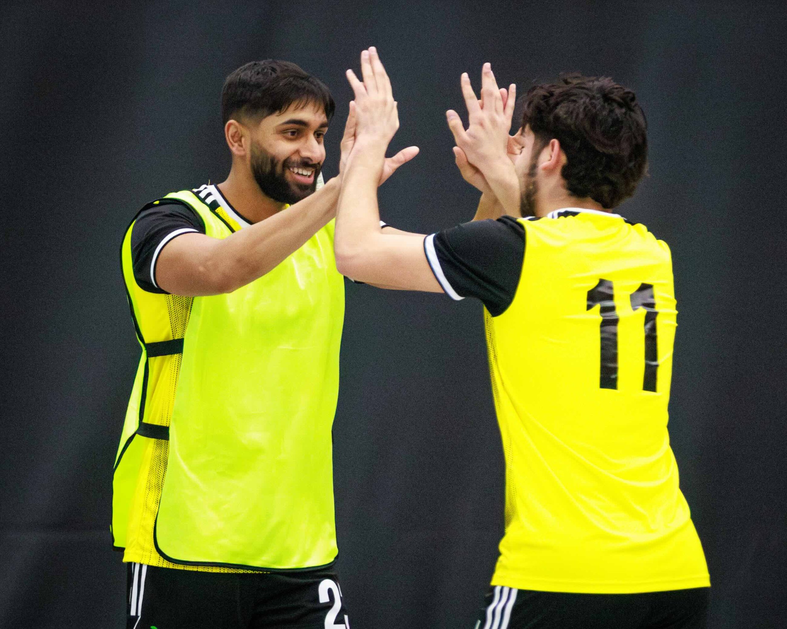Two soccer players wearing yellow jerseys with black and white accents celebrate on the field, giving high fives. One player's jersey number is 10.