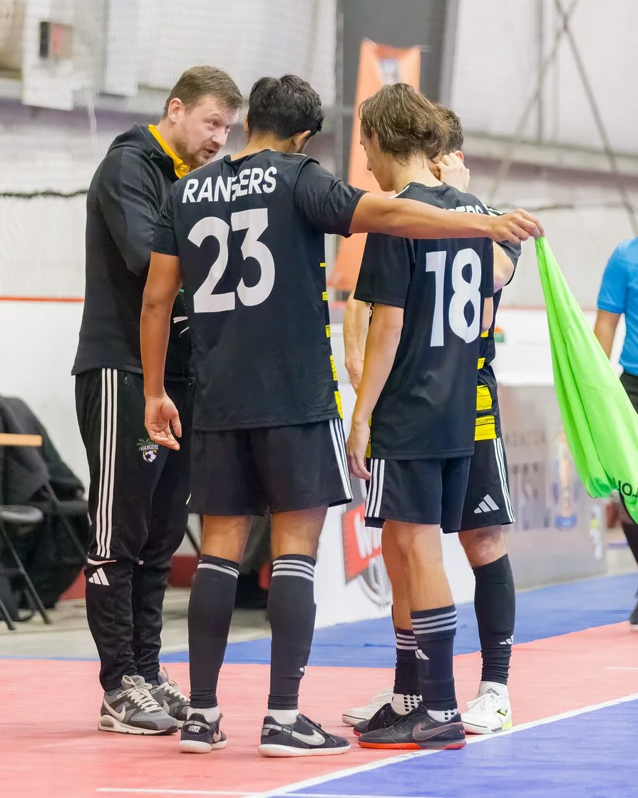 A coach giving instructions to two female volleyball players during a timeout in a game.