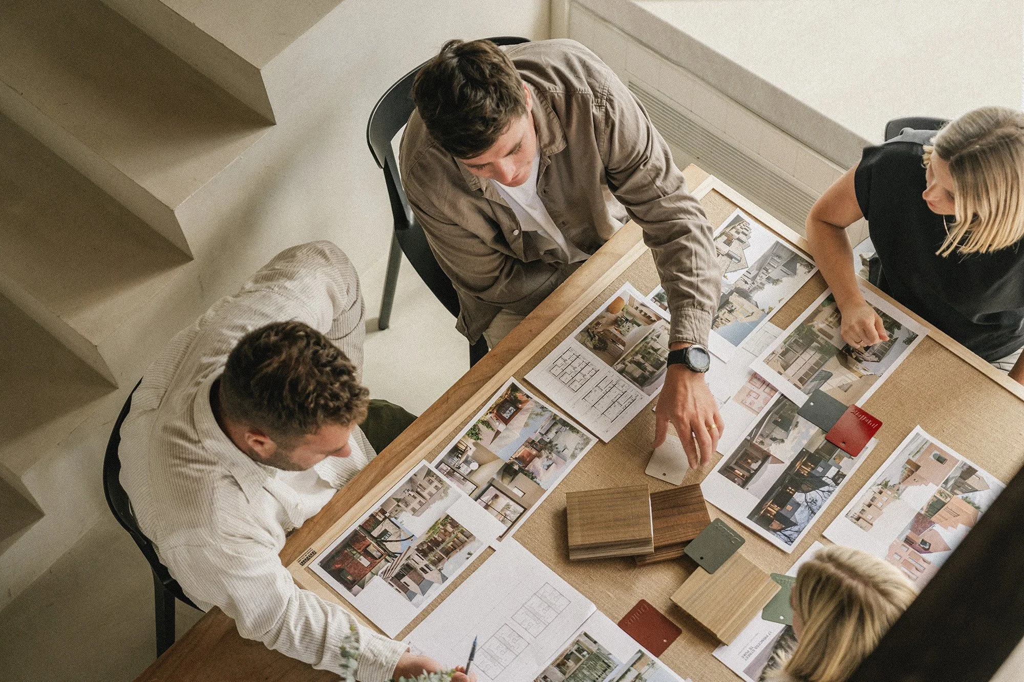 Gather Group team engaged in a discussion over interior design ideas spread across a table, featuring photos, colour samples, and design plans. Upcoming town house developments Tauranga and Mount Maungnaui.
